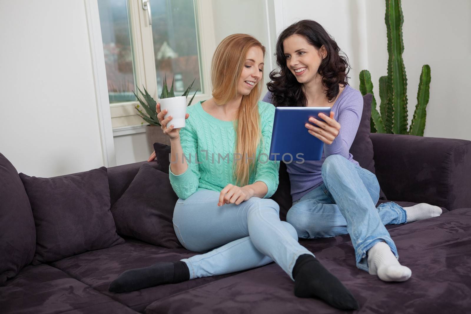 two young attractive girl with tablett pc on couch by juniart