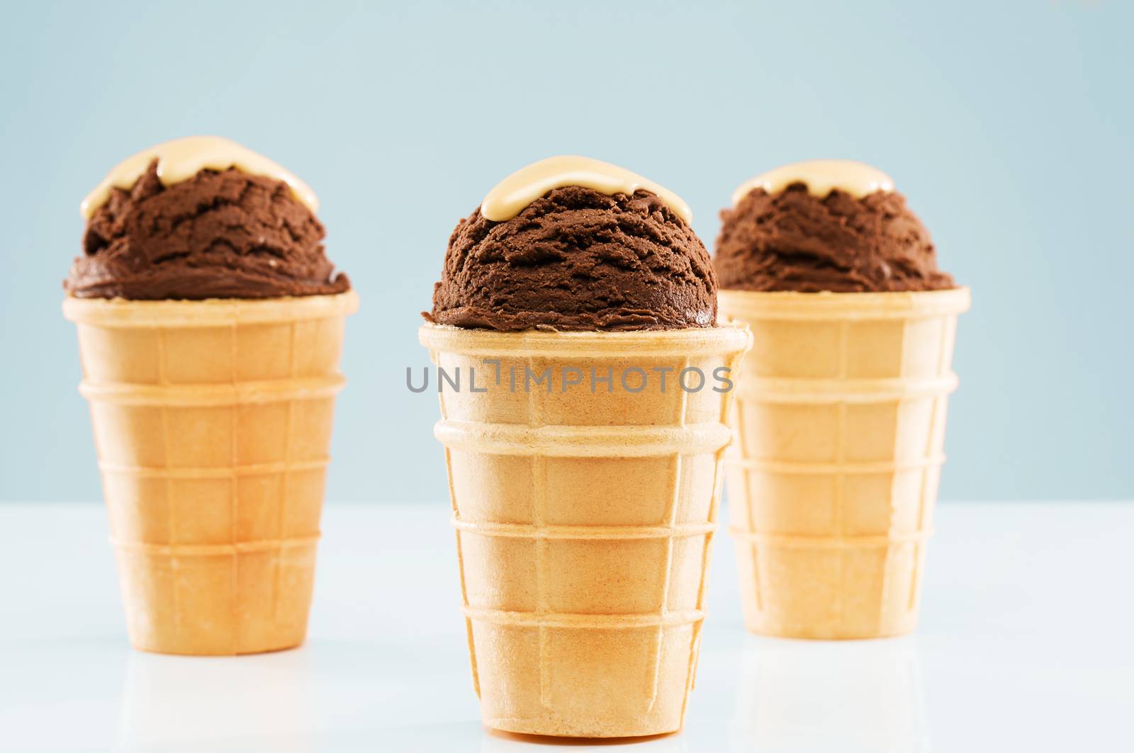 three chocolate ice cream scoops with vanilla sauce in standing waffle cones