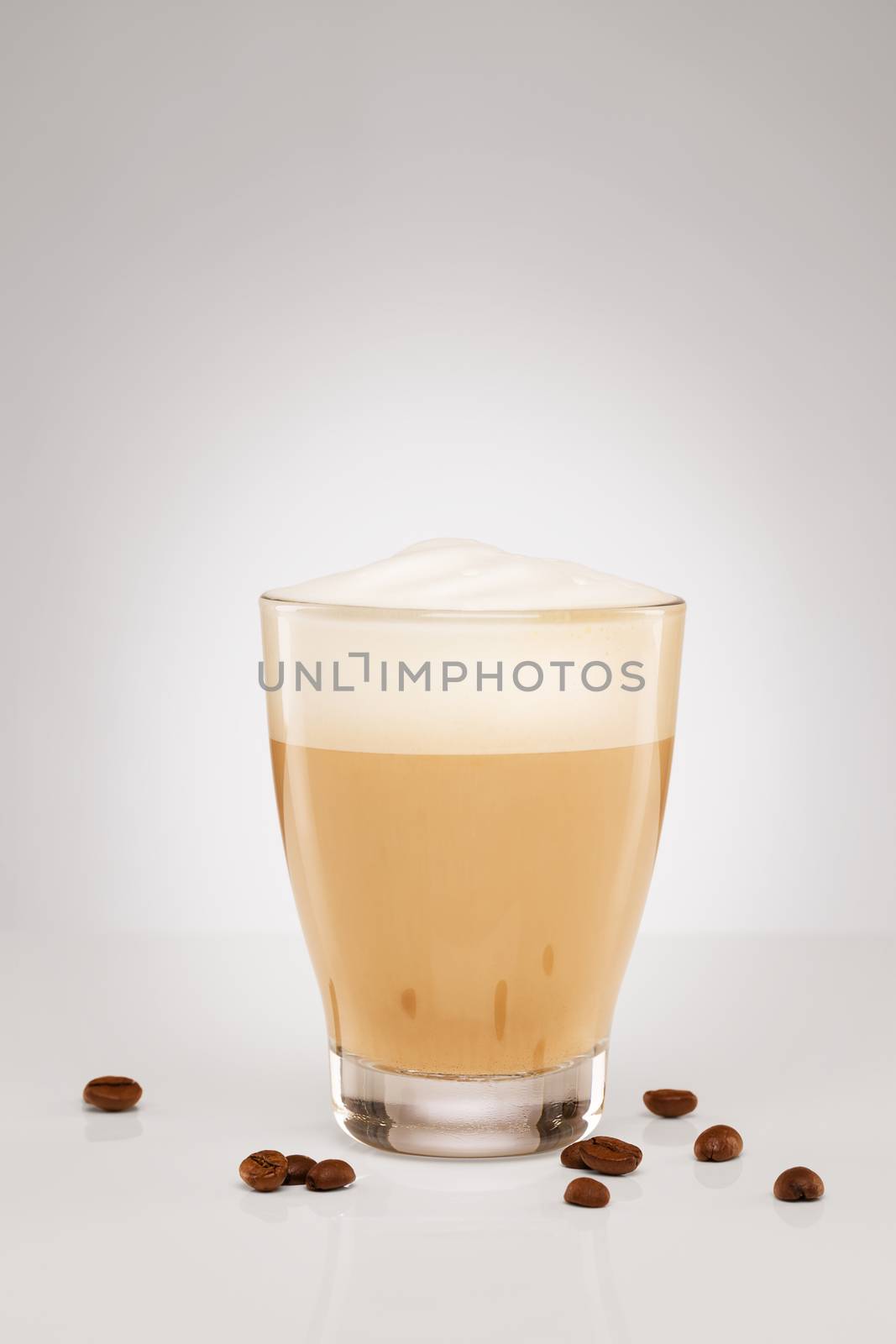 cappuccino with milk foam in a small glass with coffee beans on grey background