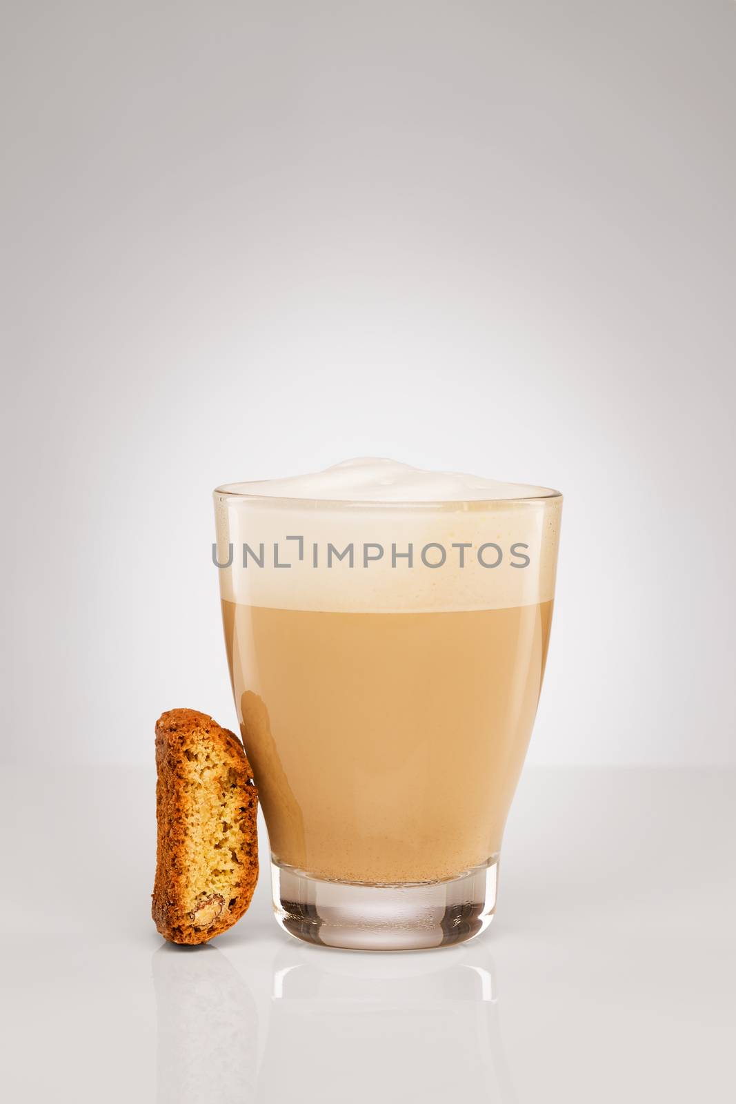 small cappuccino in a glass cup with a cantuccini cookie on gray background