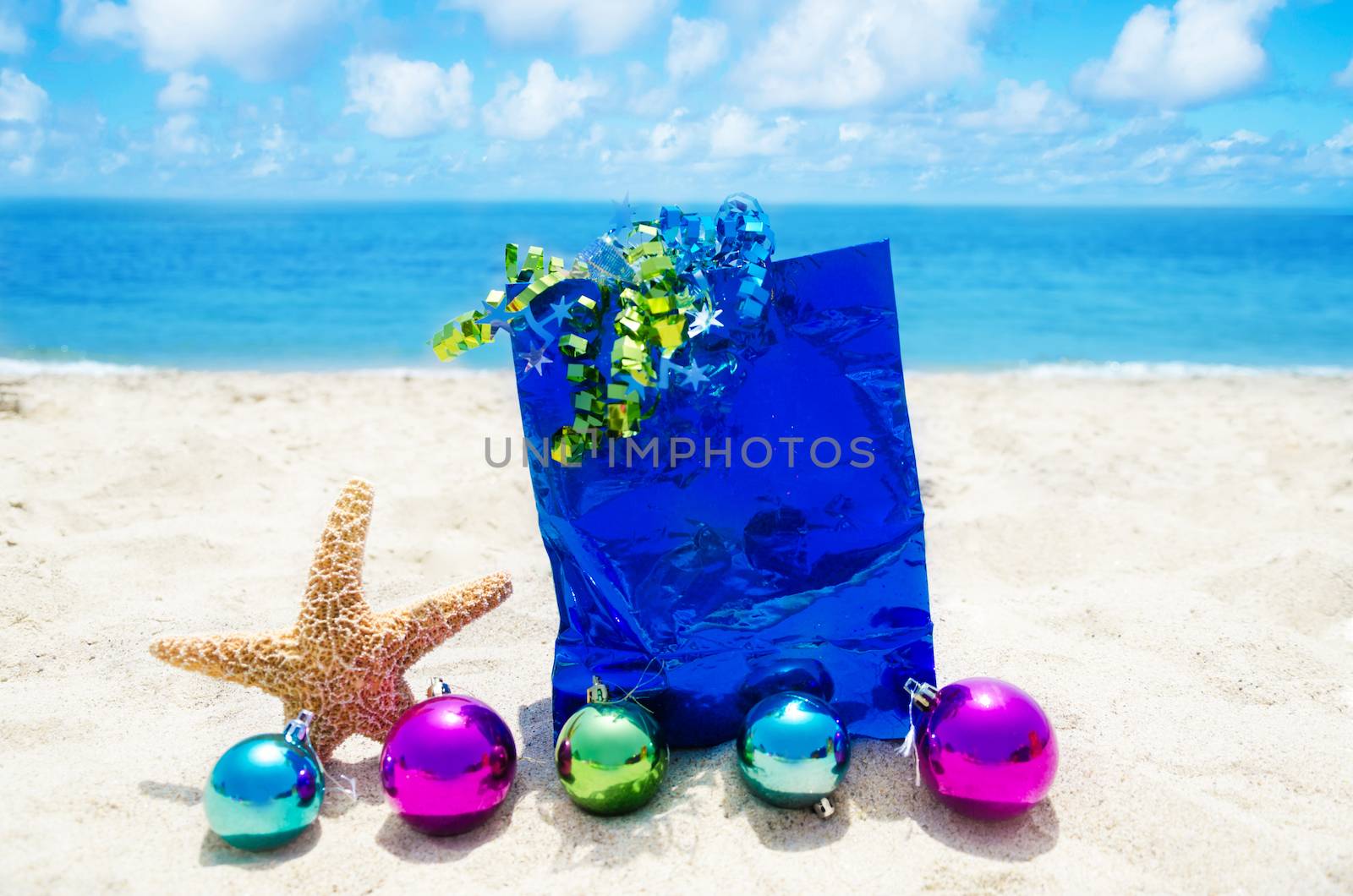 Starfish with Christmas balls and blue gift bag on sandy beach in sunny day- holiday concept