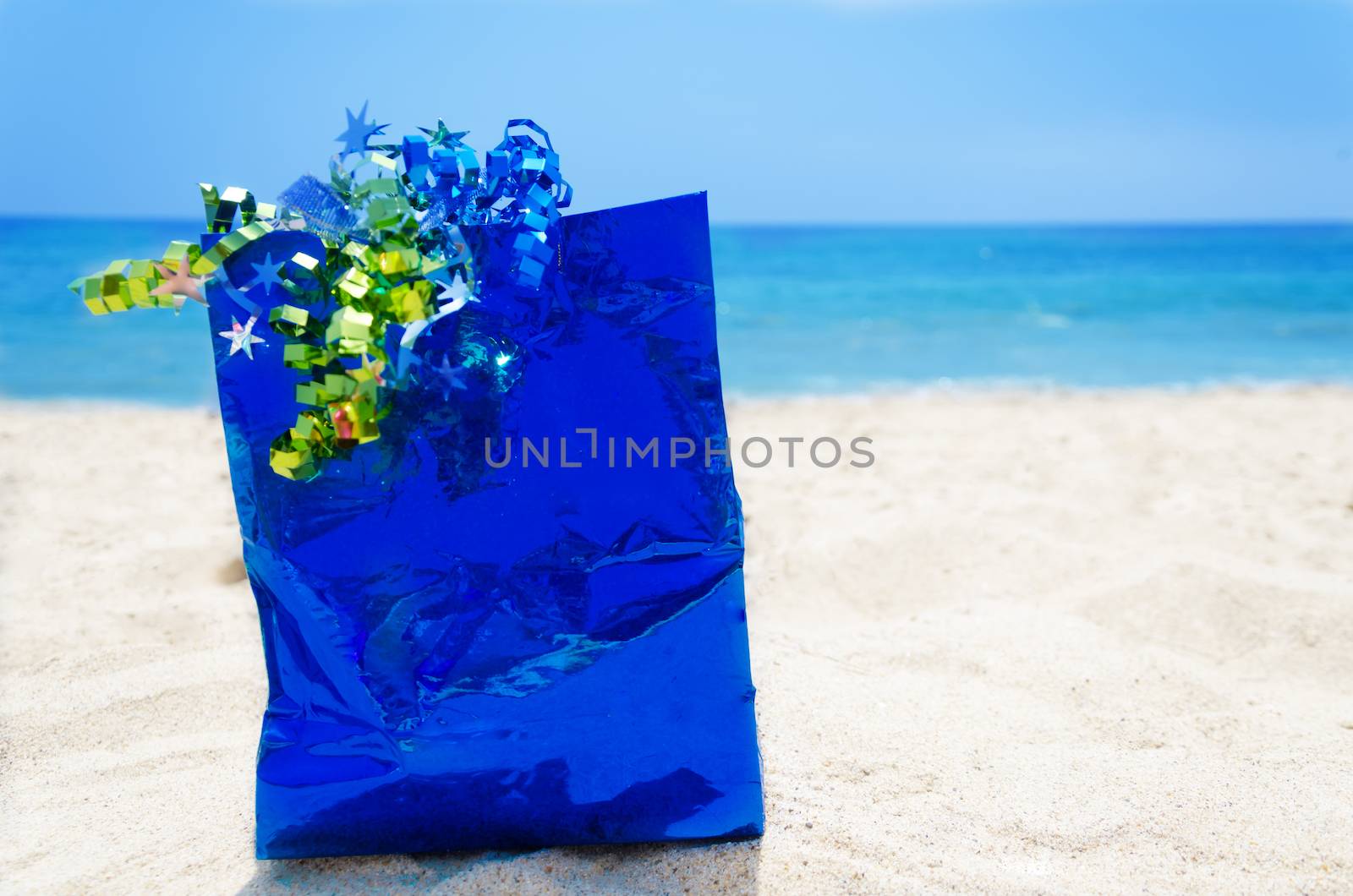 Blue gift bag on sandy beach in sunny day- holiday concept