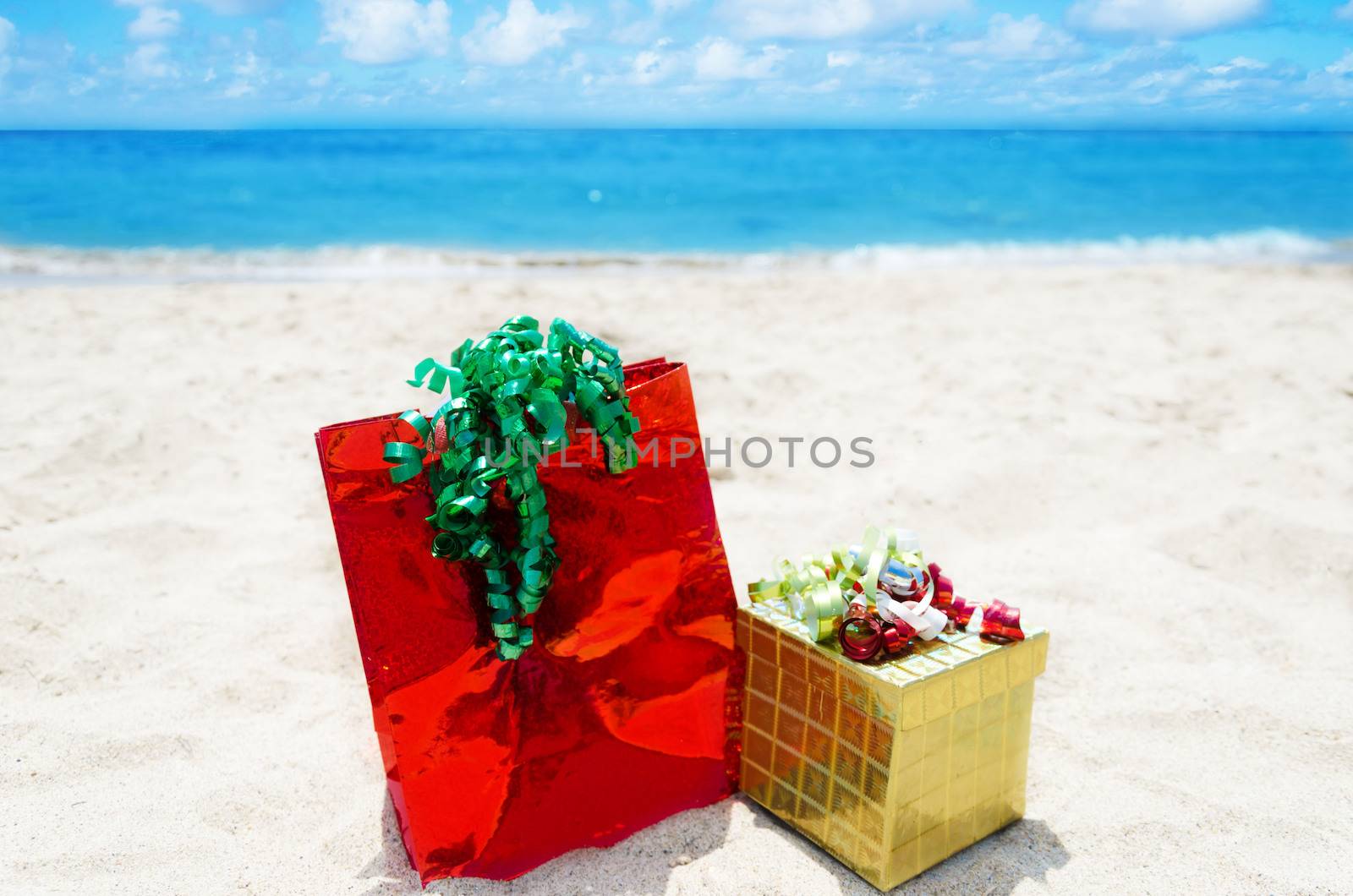 Gold gift box and red gift bag on sandy beach in sunny day- holiday concept