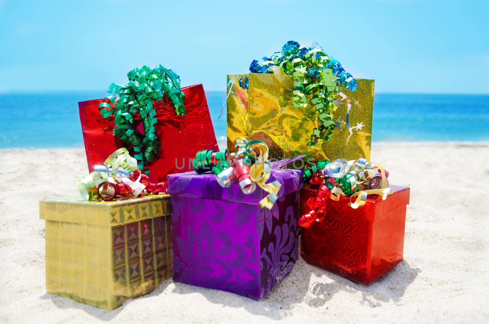 Three gift boxes and two gift bags on sandy beach in sunny day- holiday concept