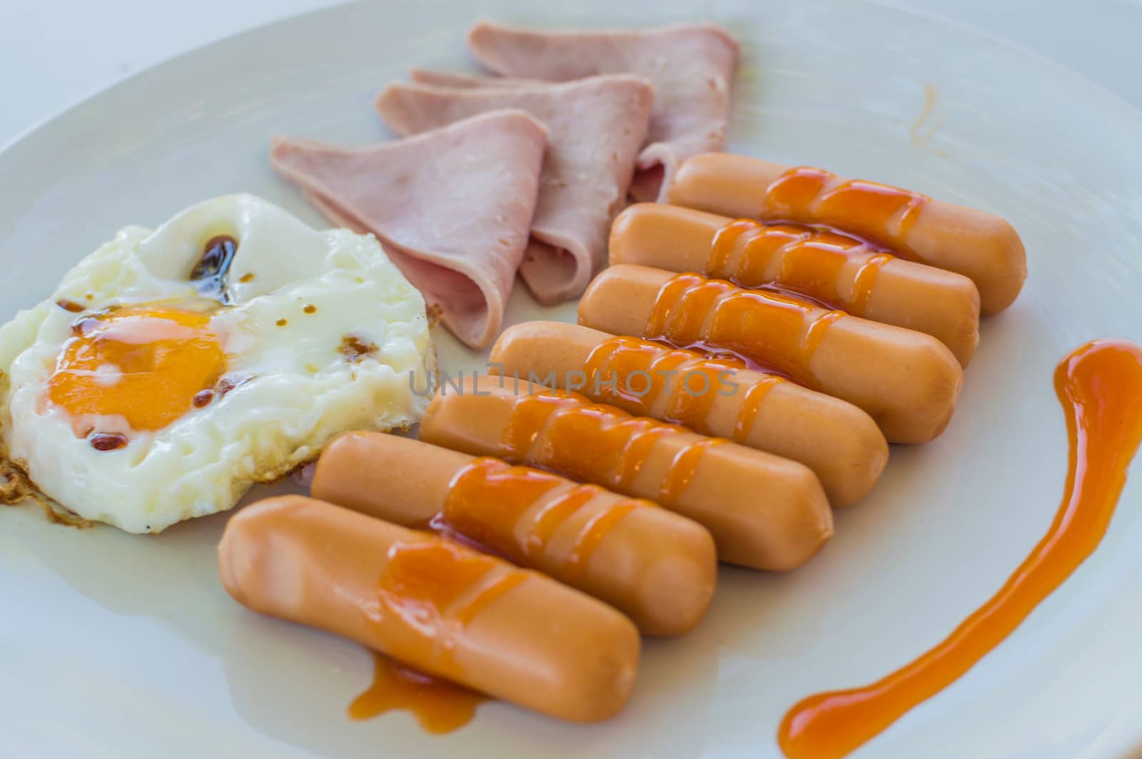Wonderful breakfast.Sausage, ham and fried egg placed on a white dish.