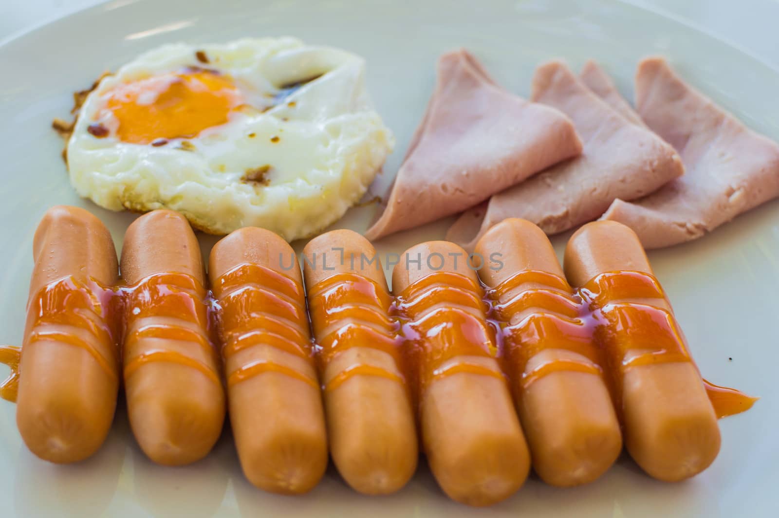 Wonderful breakfast.Sausage, ham and fried egg placed on a white dish.