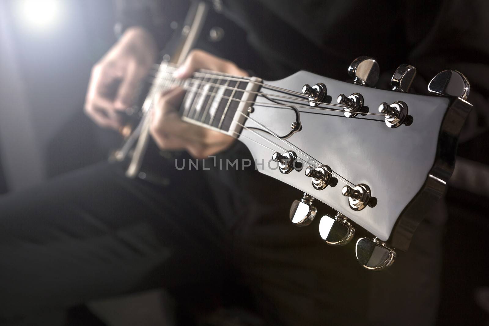 Close up of a man playing a guitar with spot light behind.