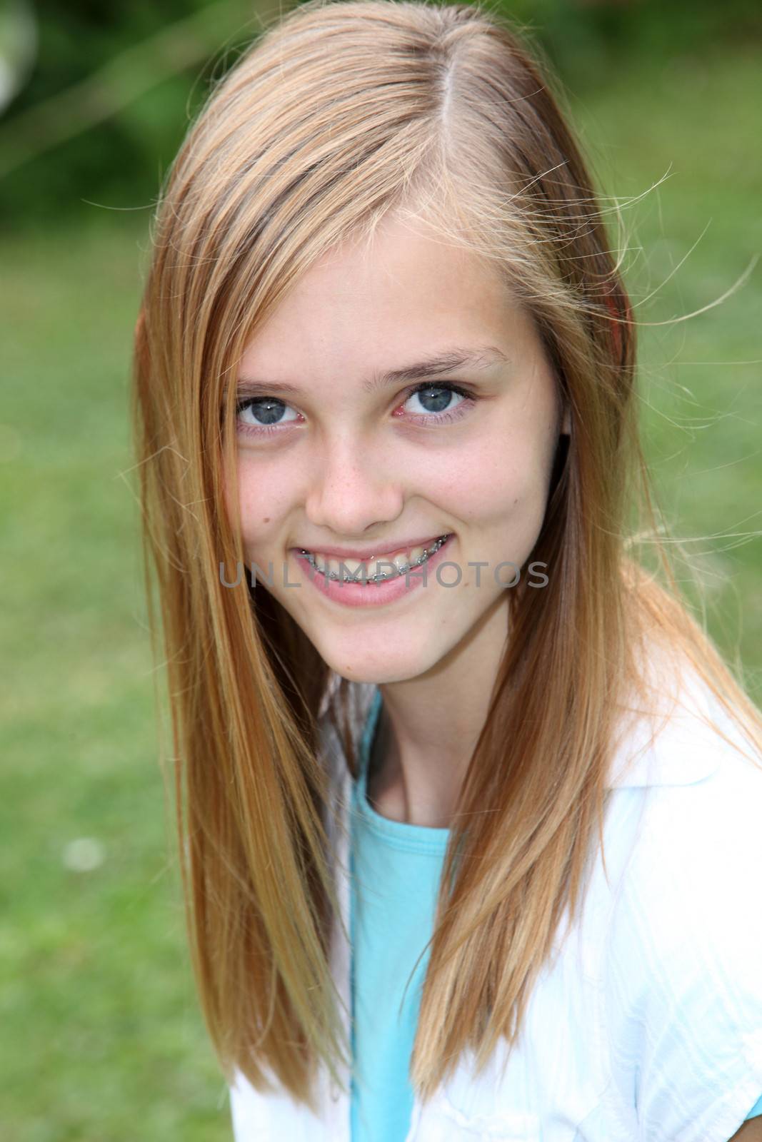 Smiling attractive young teenage girl with long blond hair and braces on her teeth looking at the camera