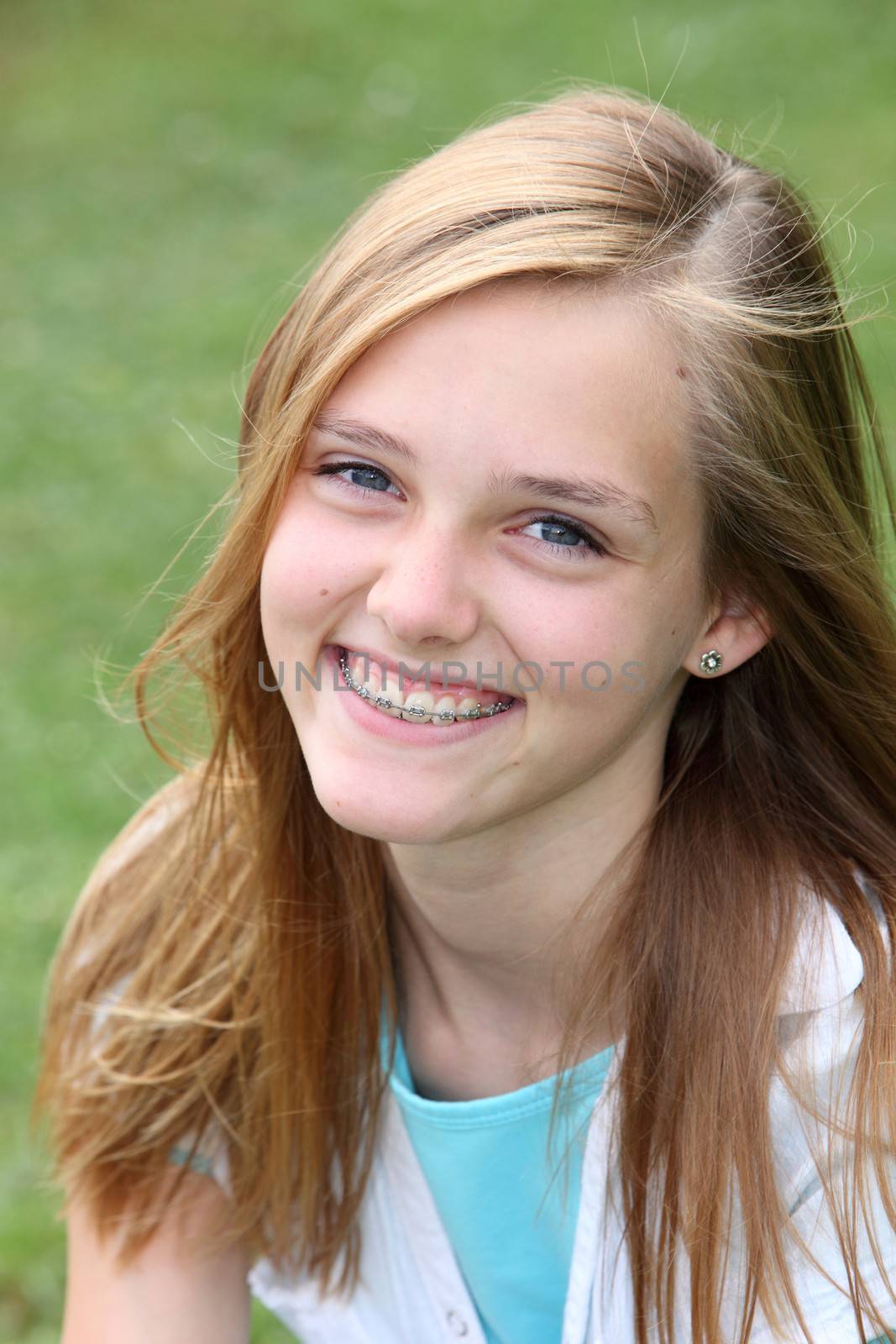 Beautiful smiling young teenager with orthodontic braces on her teeth sitting outdoors in the summer sunshine on green grass, close up head and shoulders portrait