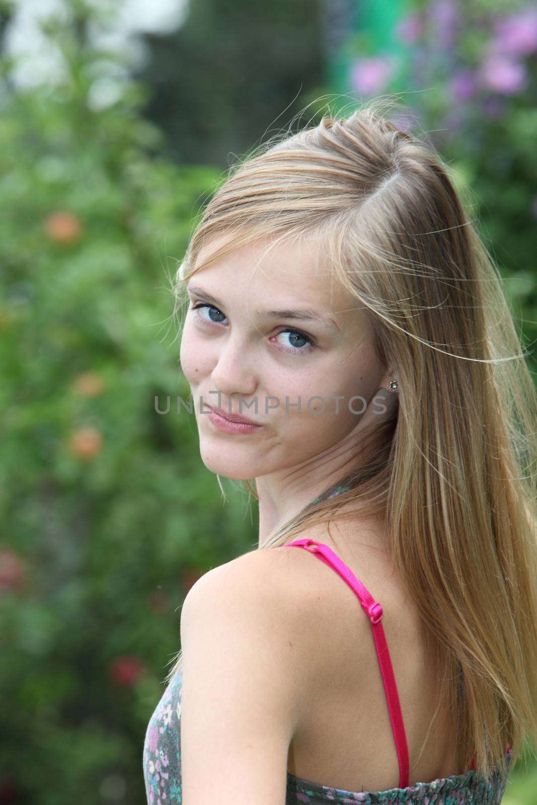 Pretty teenager looking back over her shoulder at the camera with a smile as she walks away in a summer garden