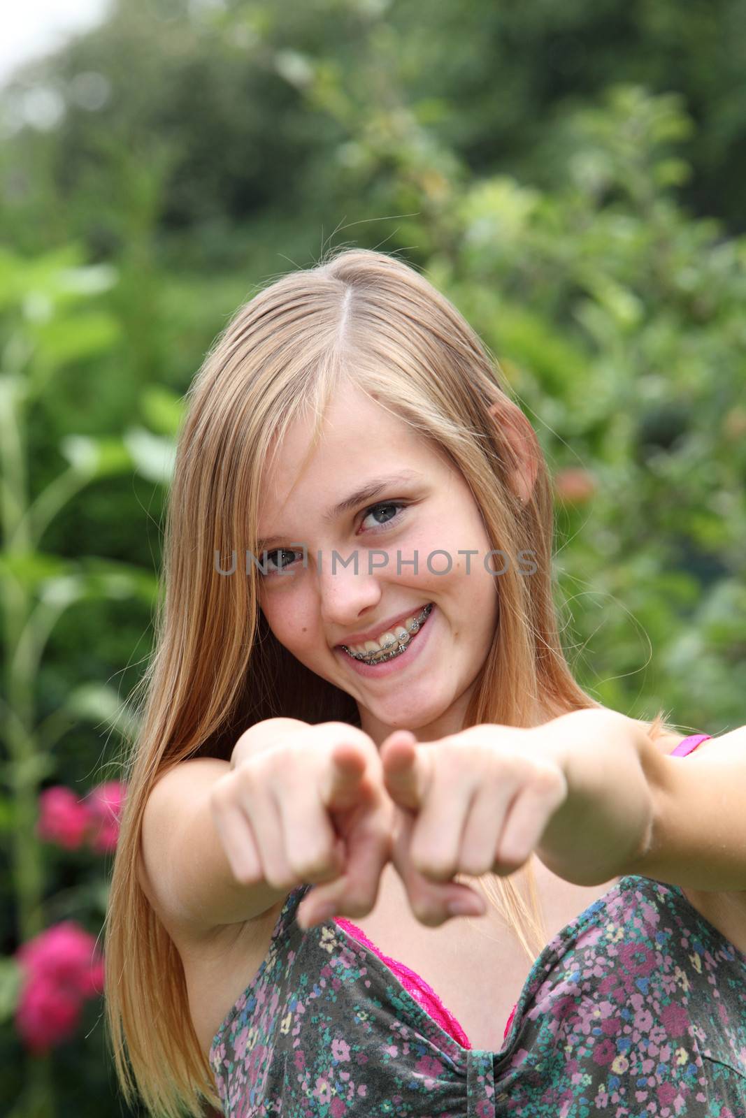 Young woman pointing her fingers at the camera with a beautiful smile on her face while standing outdoors in a garden