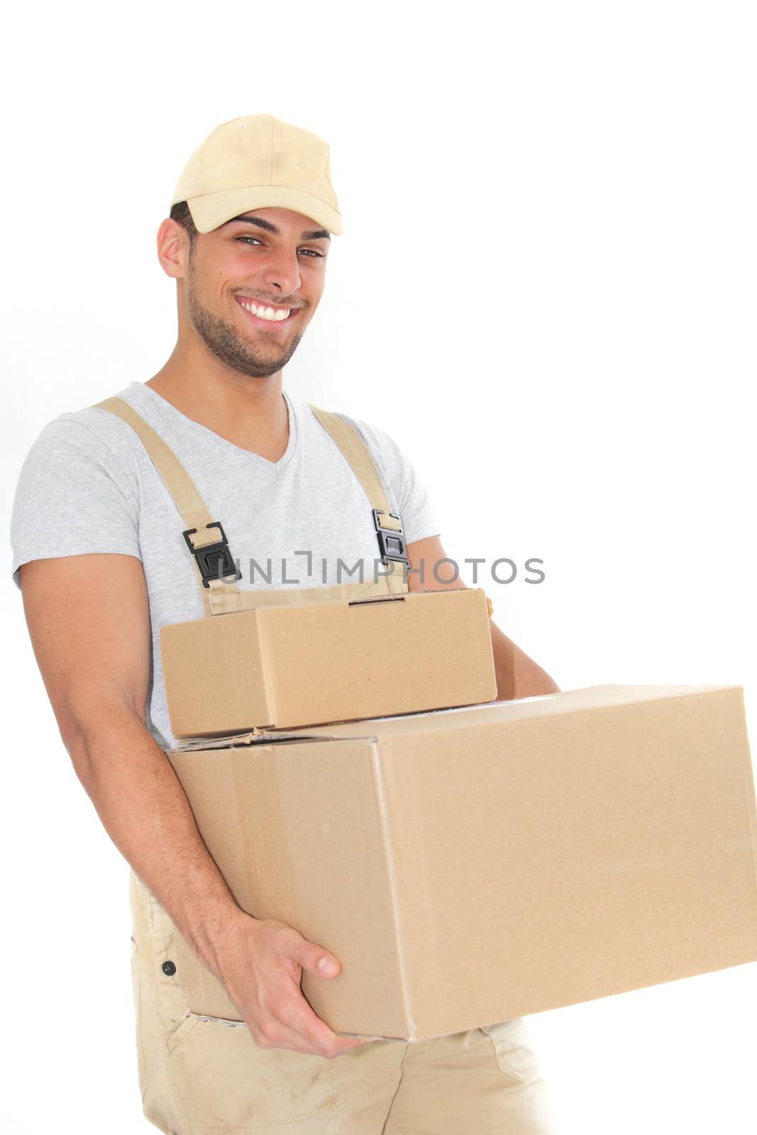 Confident young man in dungarees and a cap carrying plain brown cardboard boxes and smiling at the camera