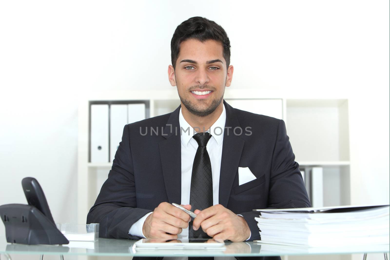 Confident successful stylish young businessman sitting at his desk with a pile of paperwork in front of him