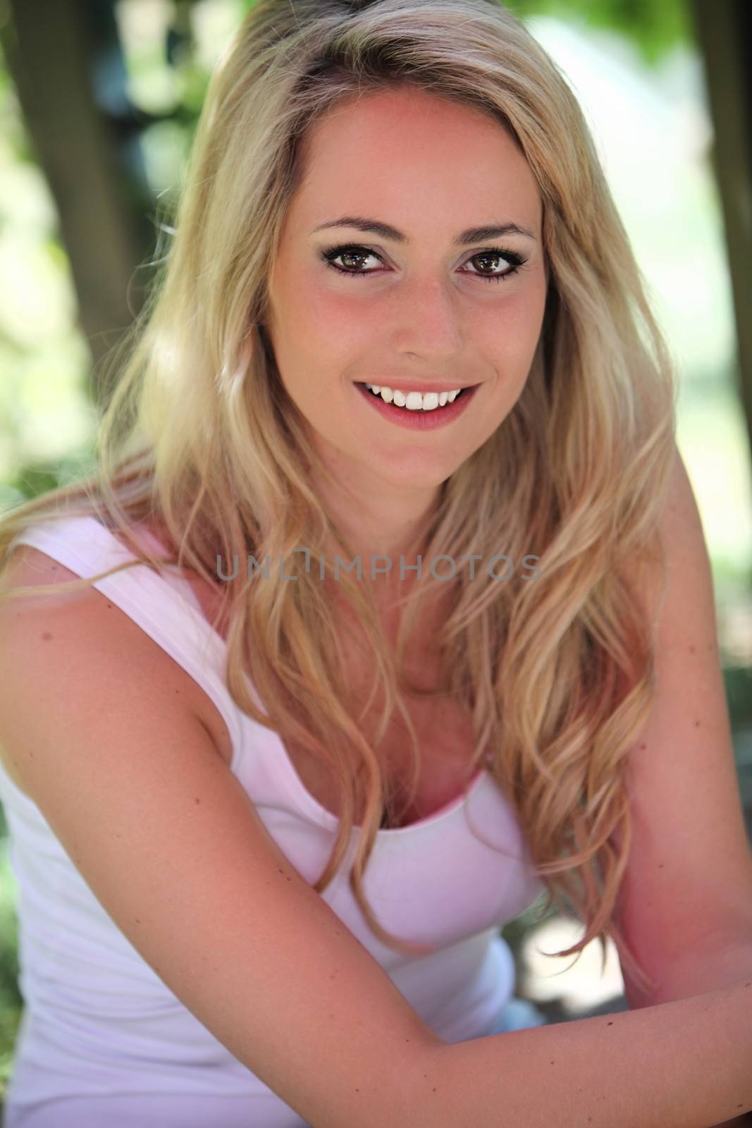 Beautiful blond woman sitting outdoors in the shade of a tree in a cool summer top