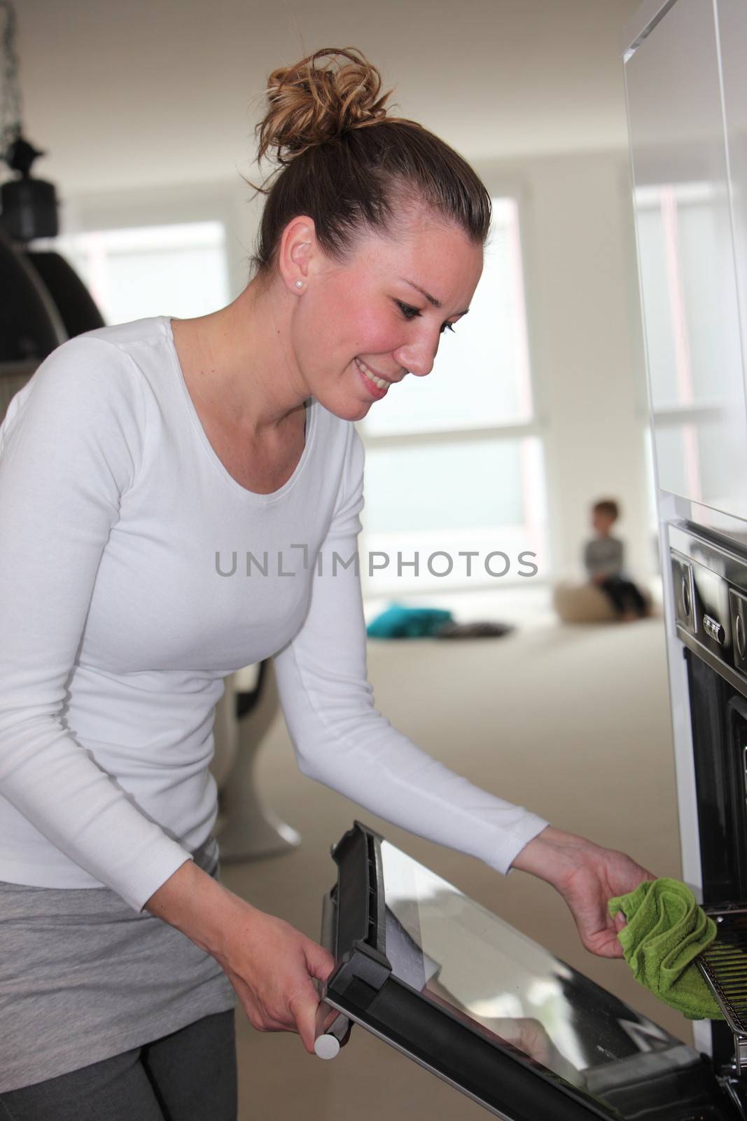 Young housewife putting food in the oven smiling as she holds the door open with a cloth in her hand