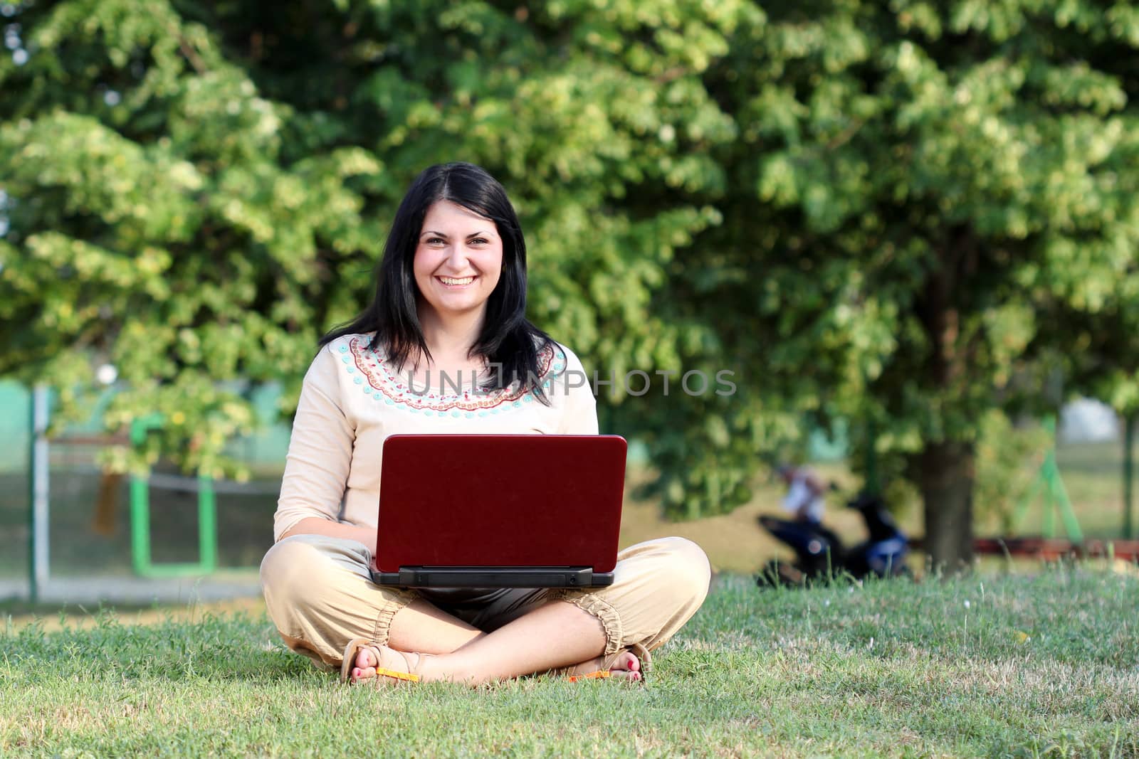 happy girl with laptop sitting on grass