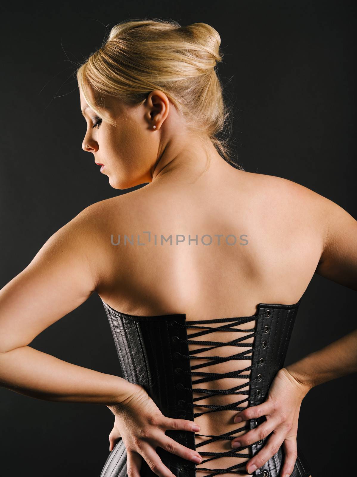 Photo of the back of a beautiful blond woman wearing a leather coset.
