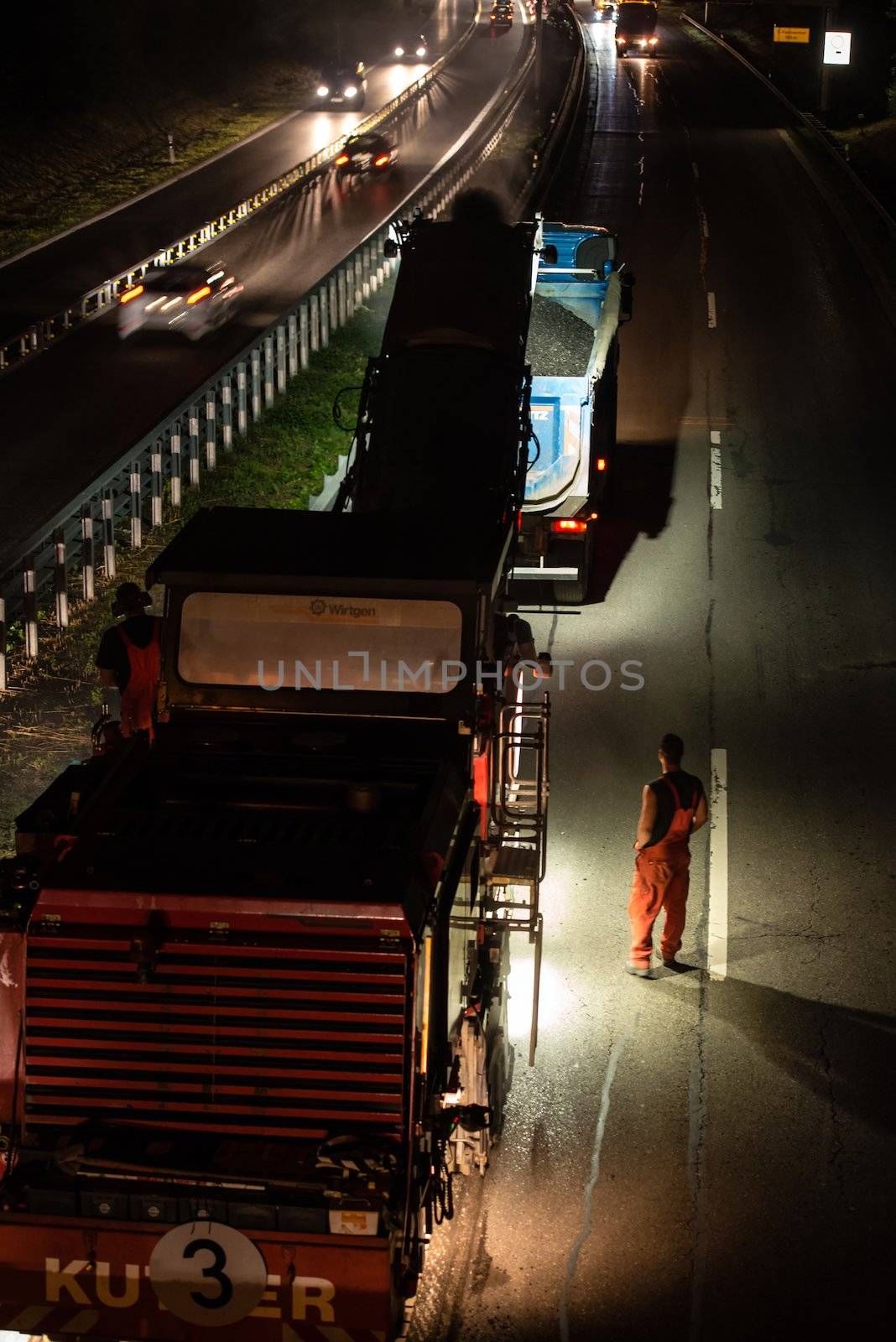 STUTTGART, GERMANY - AUGUST 16 ,2013: Workers removing asphalt on a public interstate (B27) using heavy machinery during holiday season on the evening of August 16, 2013 in Stuttgart, Germany.