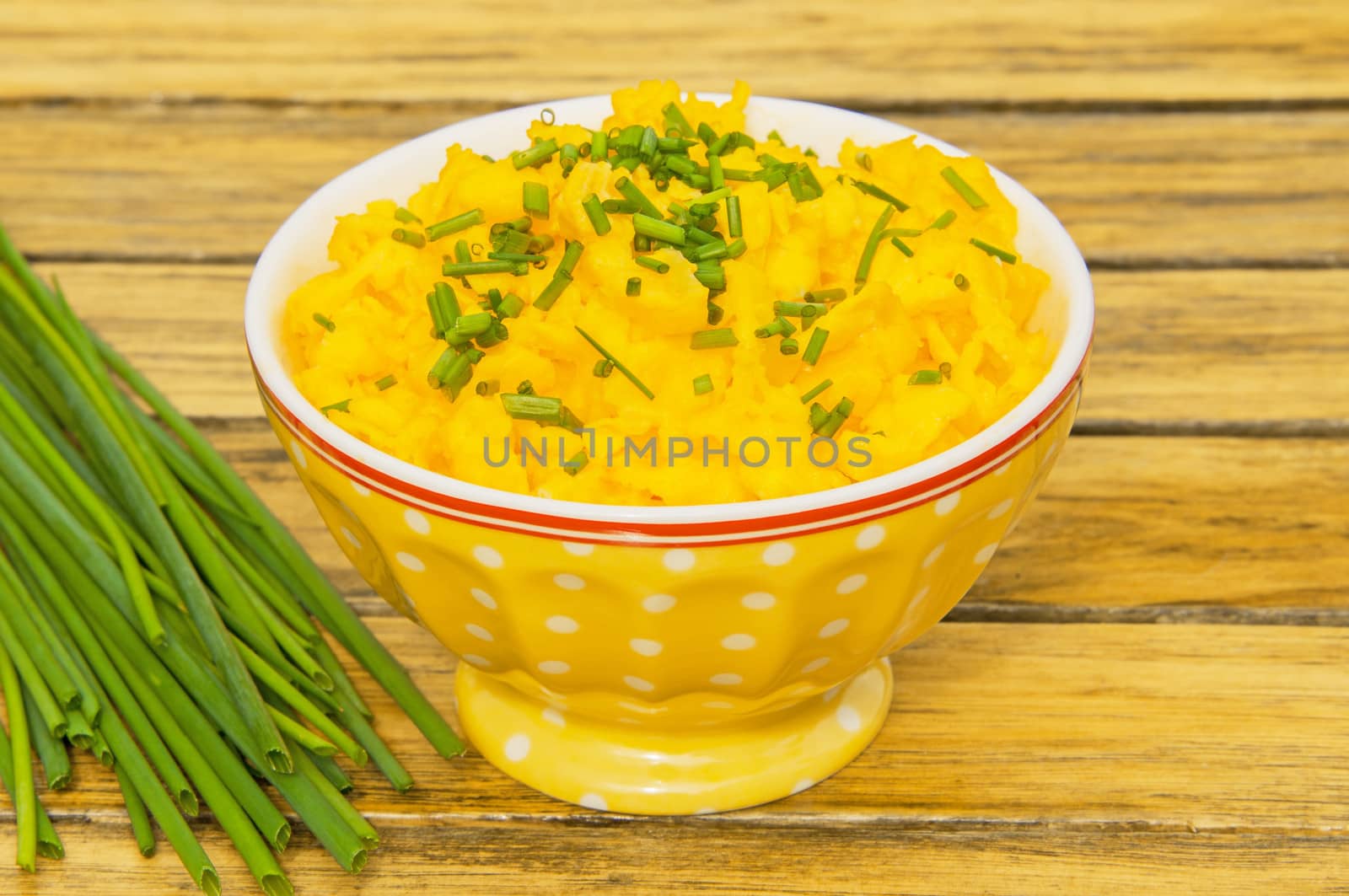 Scrambled eggs with chives in a yellow bowl on a wooden table