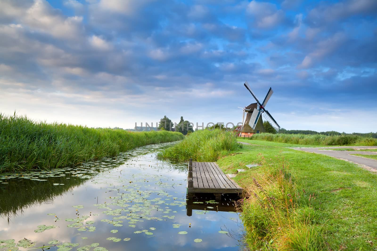 Dutch windmill by river with reflected blue sky, Groningen, Netherlands