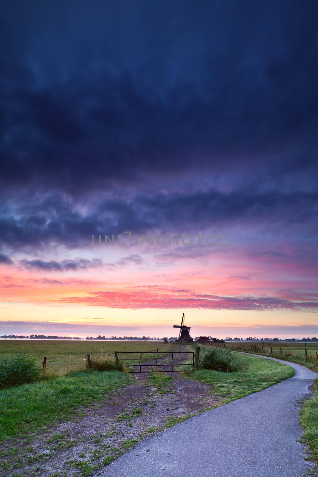 bicycle road to Dutch windmill in dramatic sunrise