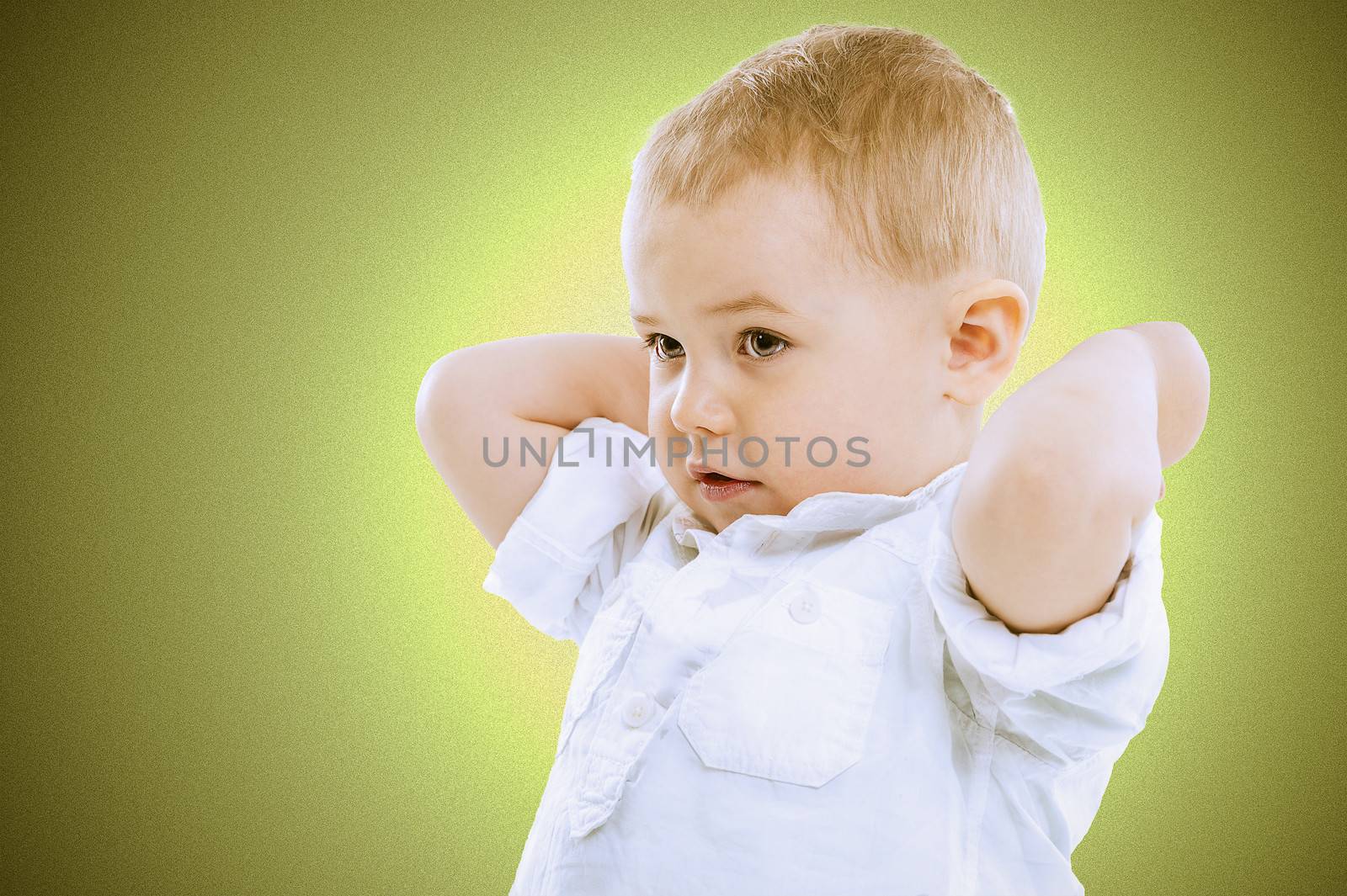 Cute handsome little blond boy with raised arms standing looking towards the left of the frame against a graduated green background with vignetting