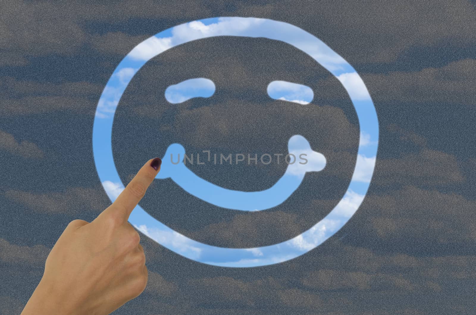 hand drawing a smiley face on a dirty window with a finger revealing clear blue sky on the other side