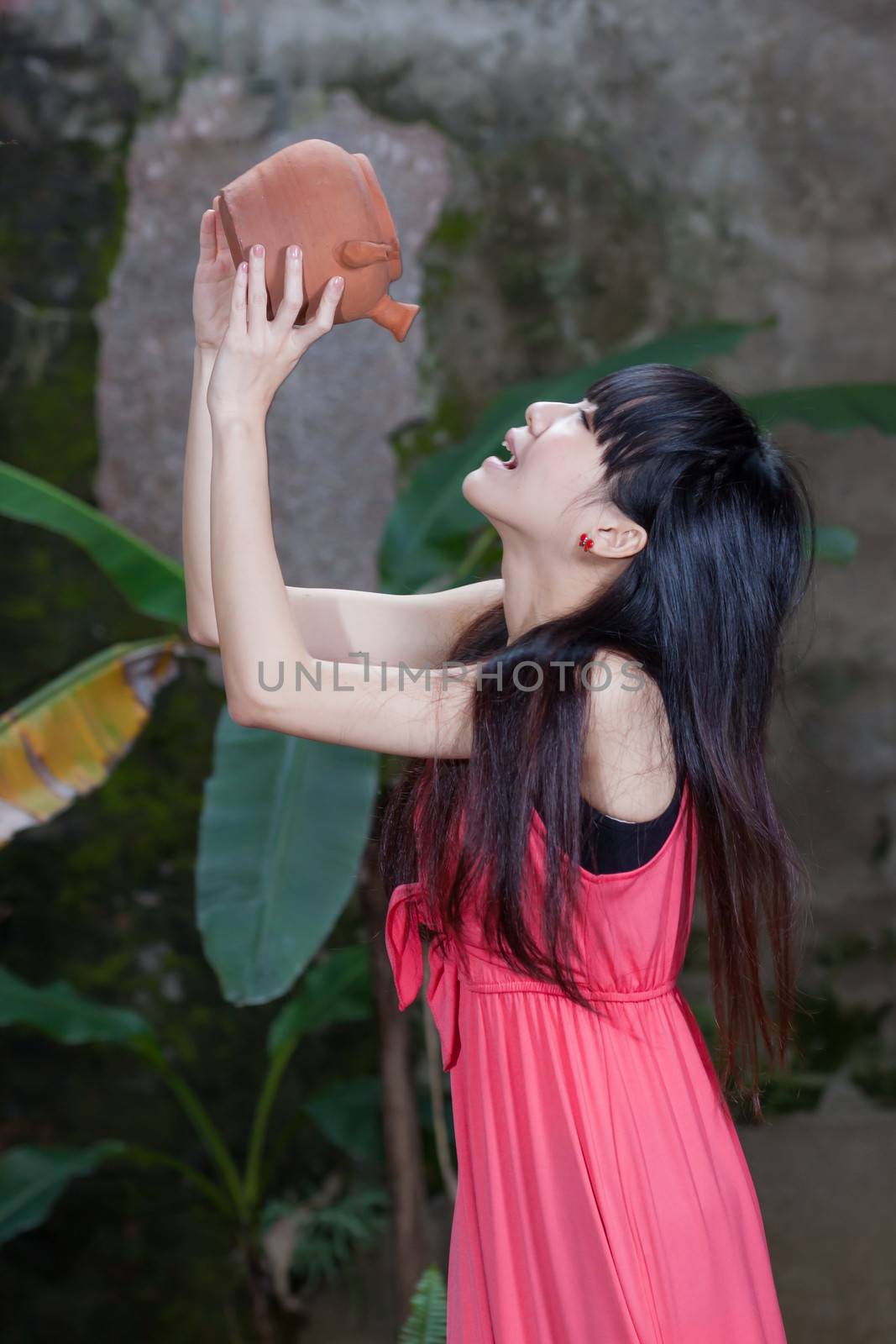 Asian girl by foliage drinking from clay pot