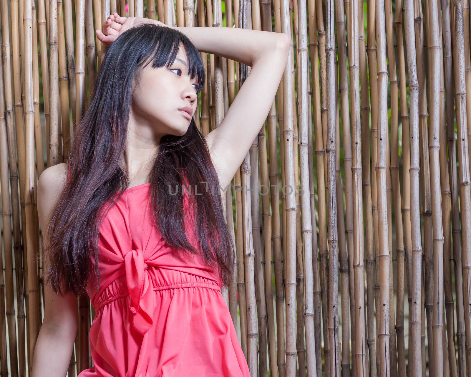 Asian girl sitting against bamboo wall