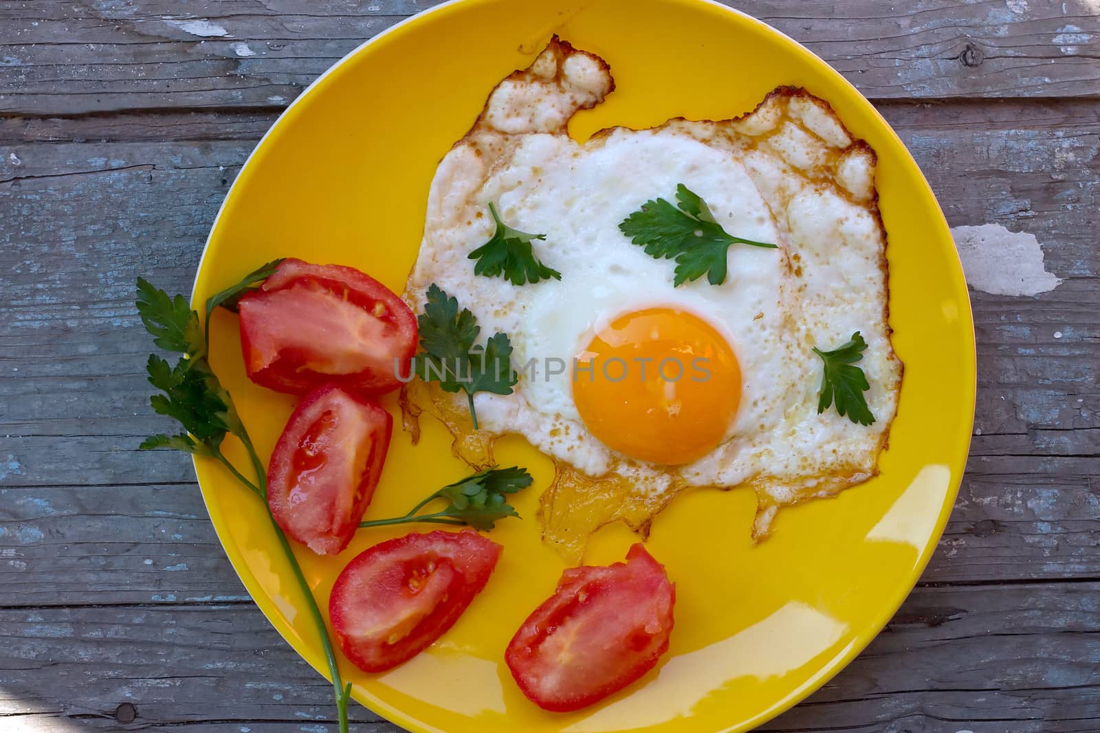 Scrambled eggs with tomato in a yellow plate on the old board