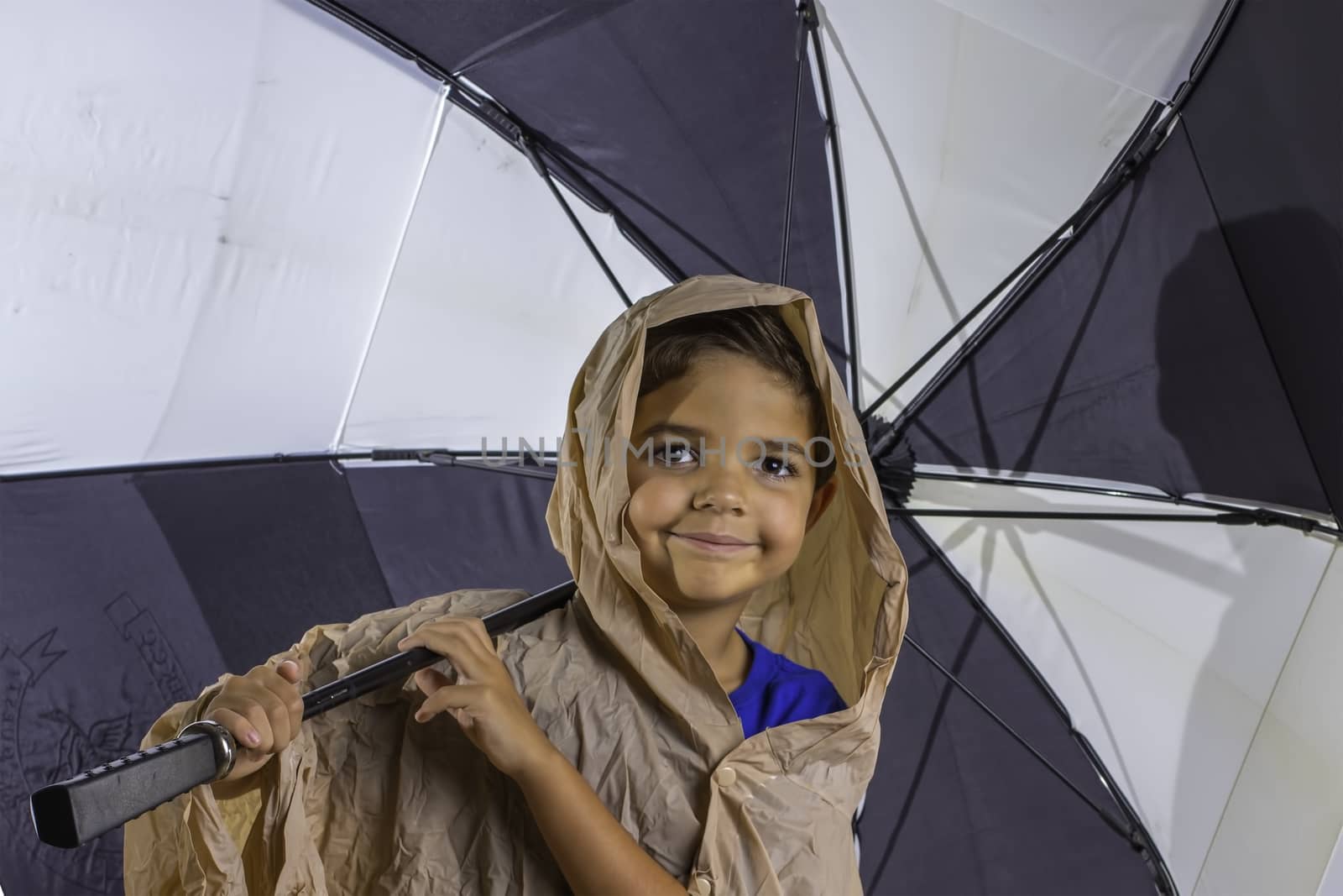 A young boy wearing a poncho and carryinga large black and white umbrella.