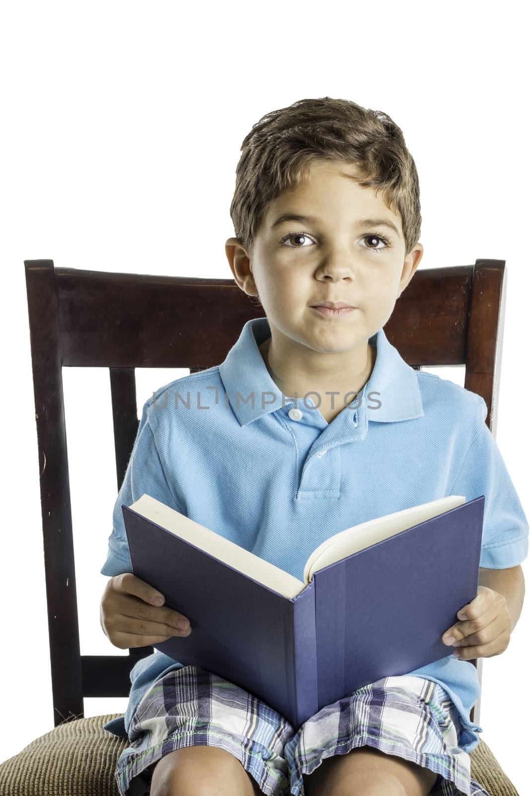 A young boy sitting in a chair reading a book.