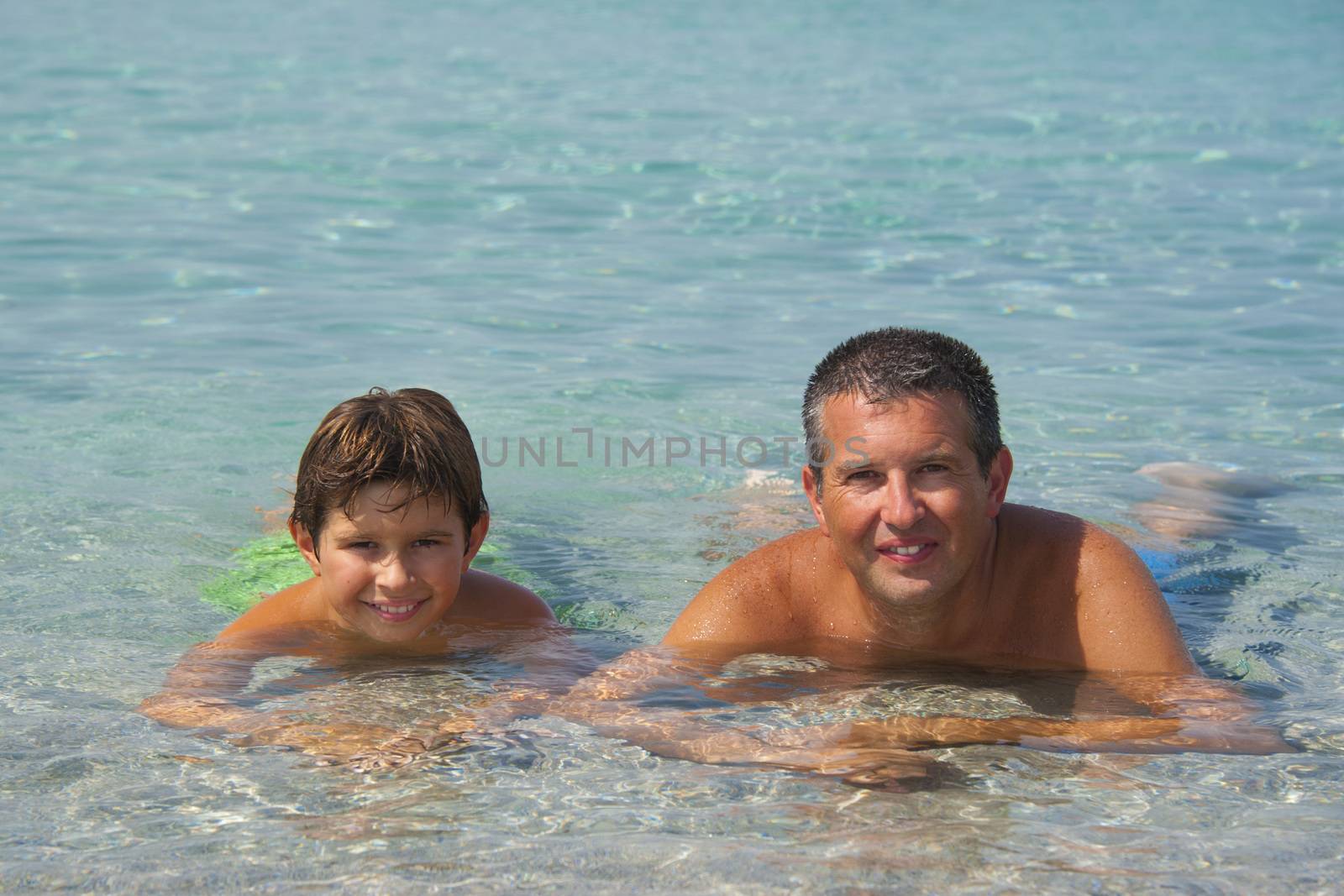 Father and son liying in the sea in Sardinia