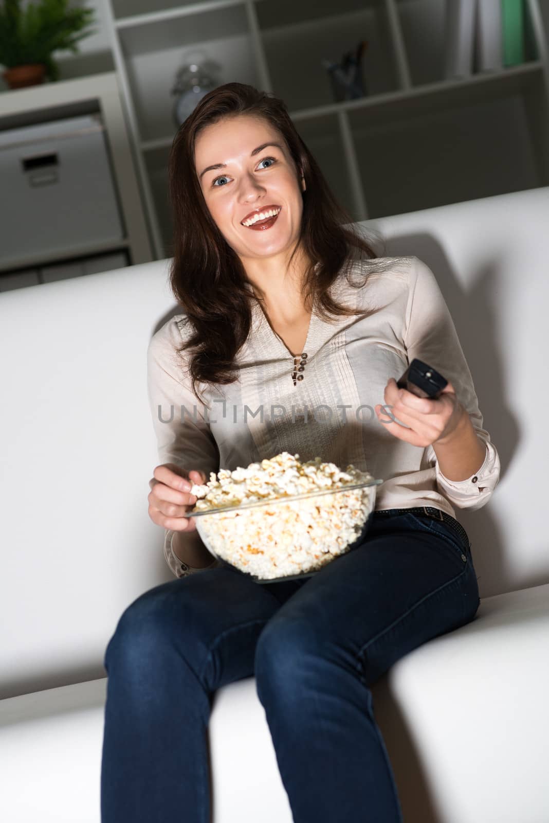 Young woman watching TV on the couch, eating popcorn