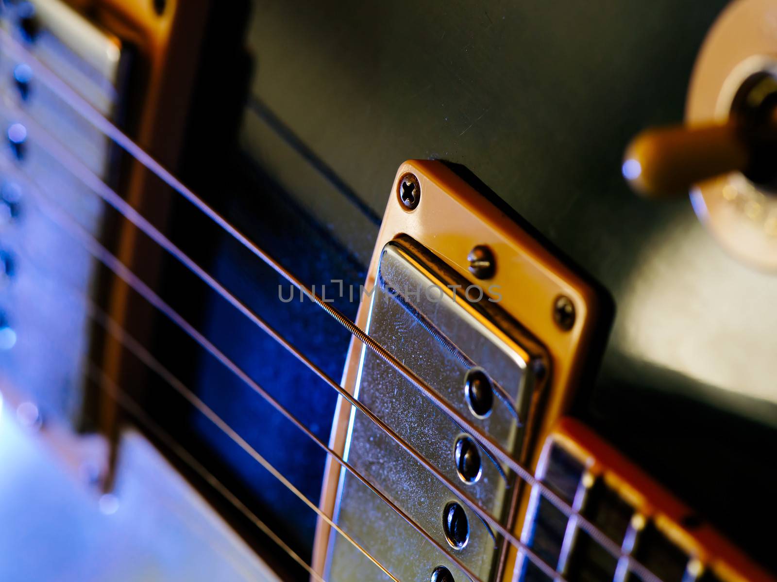 Macro abstract photo of the pickups and strings of an electric guitar. Shallow depth of field with focus on the first string.