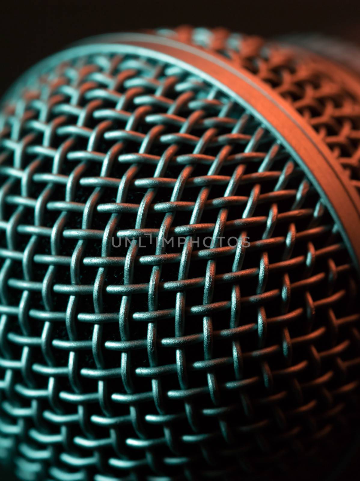 Macro photo of a vocal microphone lit with stage lights.