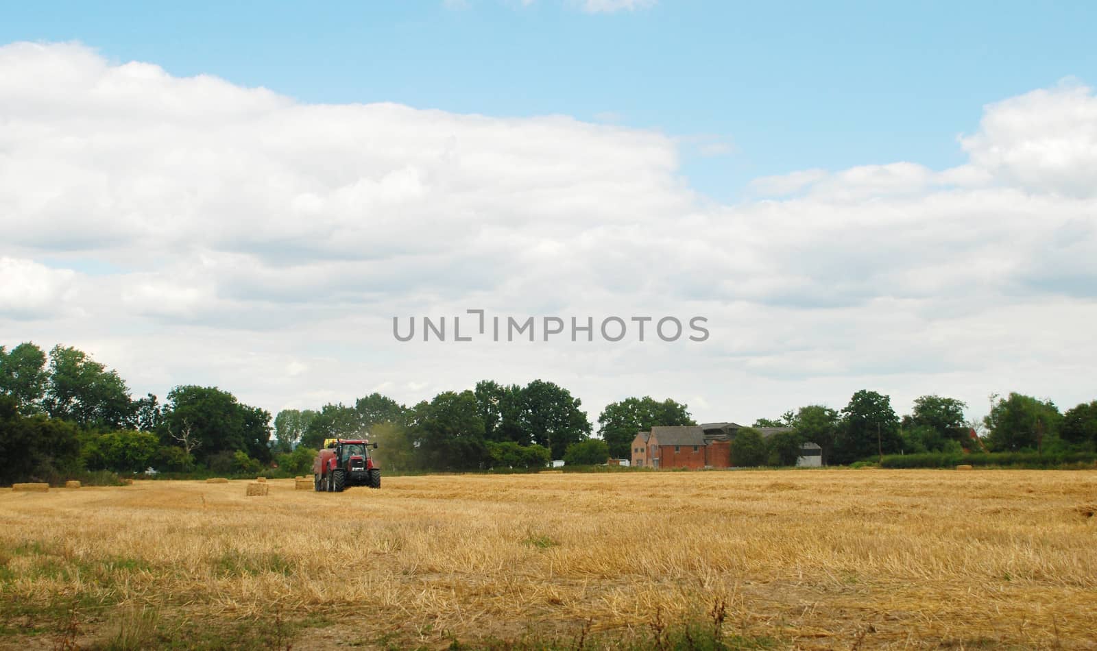 Red tractor baling cut straw in an English farm field 
