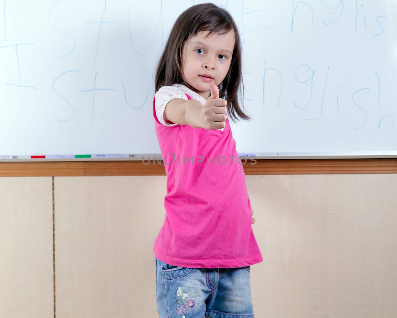 Child at whiteboard writing I study English with a thumbs up