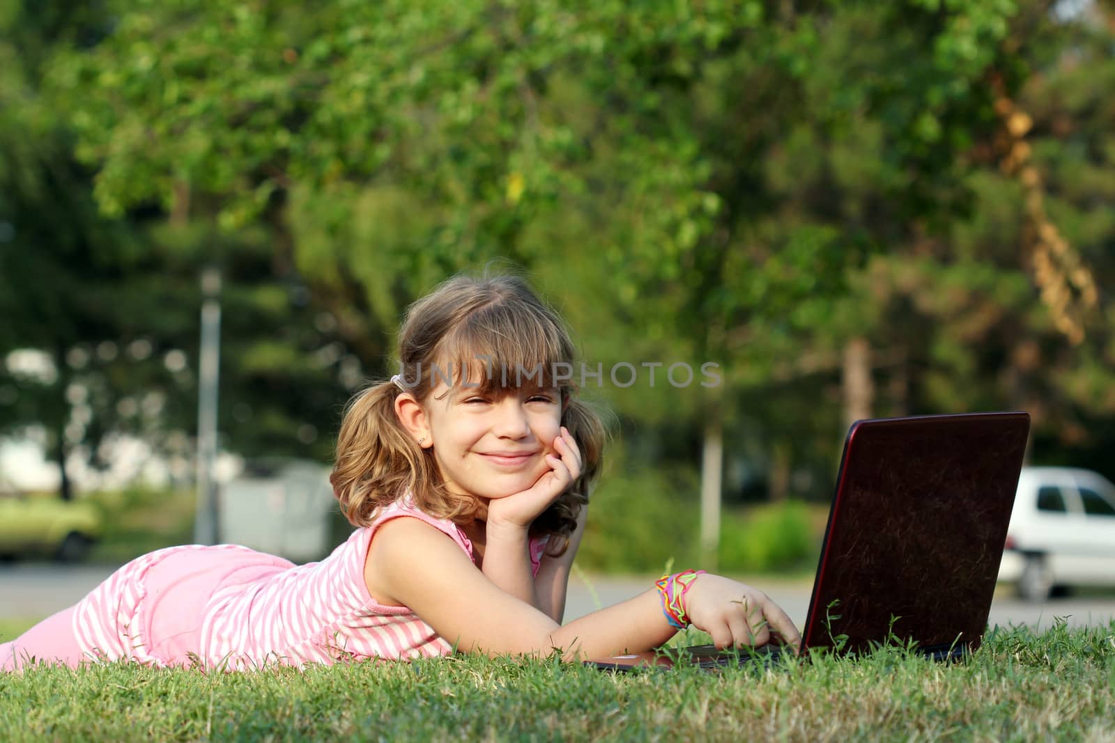 happy little girl with laptop lying on grass