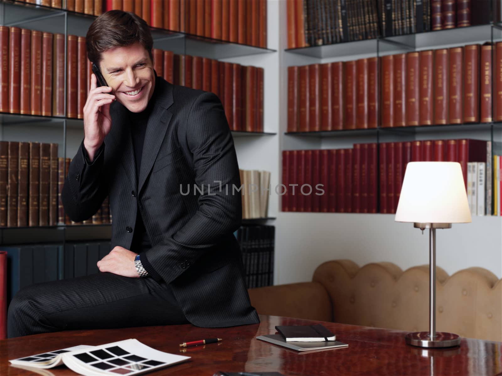 Businessman working at office desk, talking on mobile phone