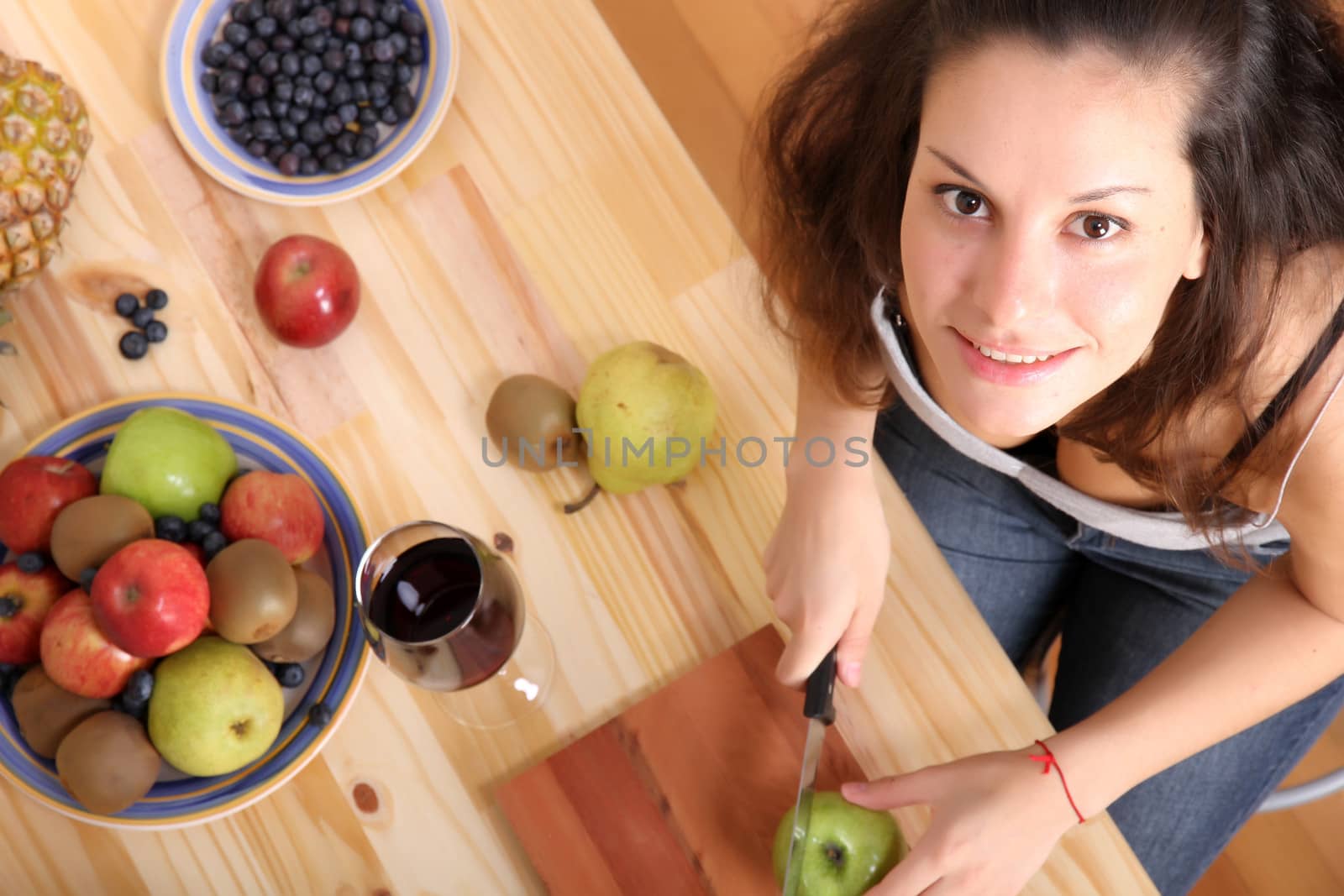 A young adult woman cutting fruits in the kitchen.