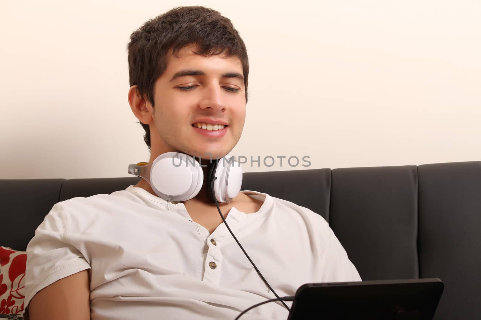 A young, latin man with a Tablet PC and Headphones on the Sofa
