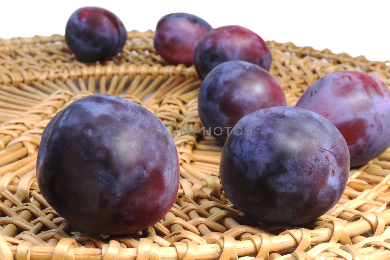 Large ripe purple plum wicker dish. Presented on a white background.