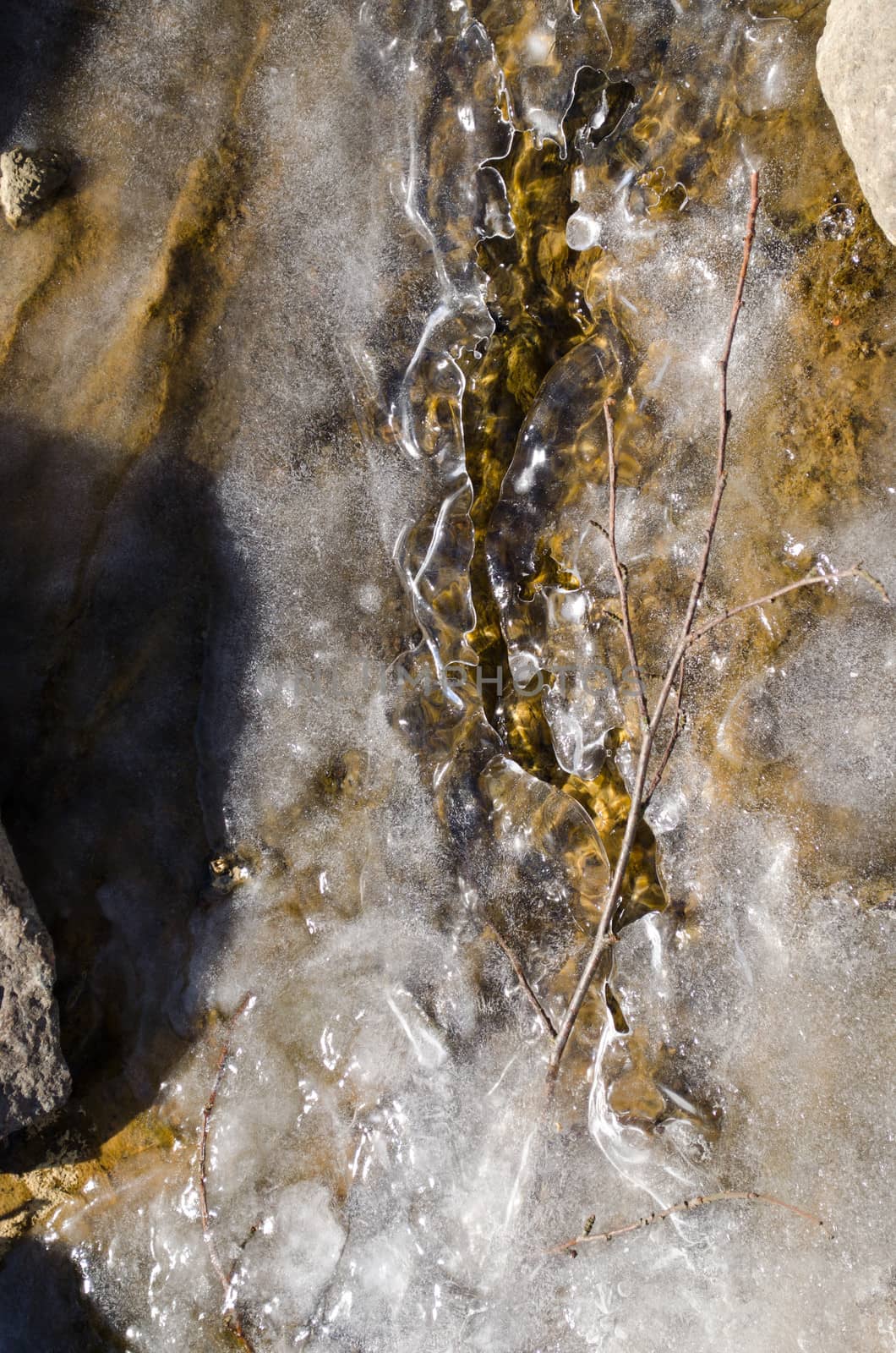 frozen small forest stream water flow between stones sunlight reflection ice in winter season.