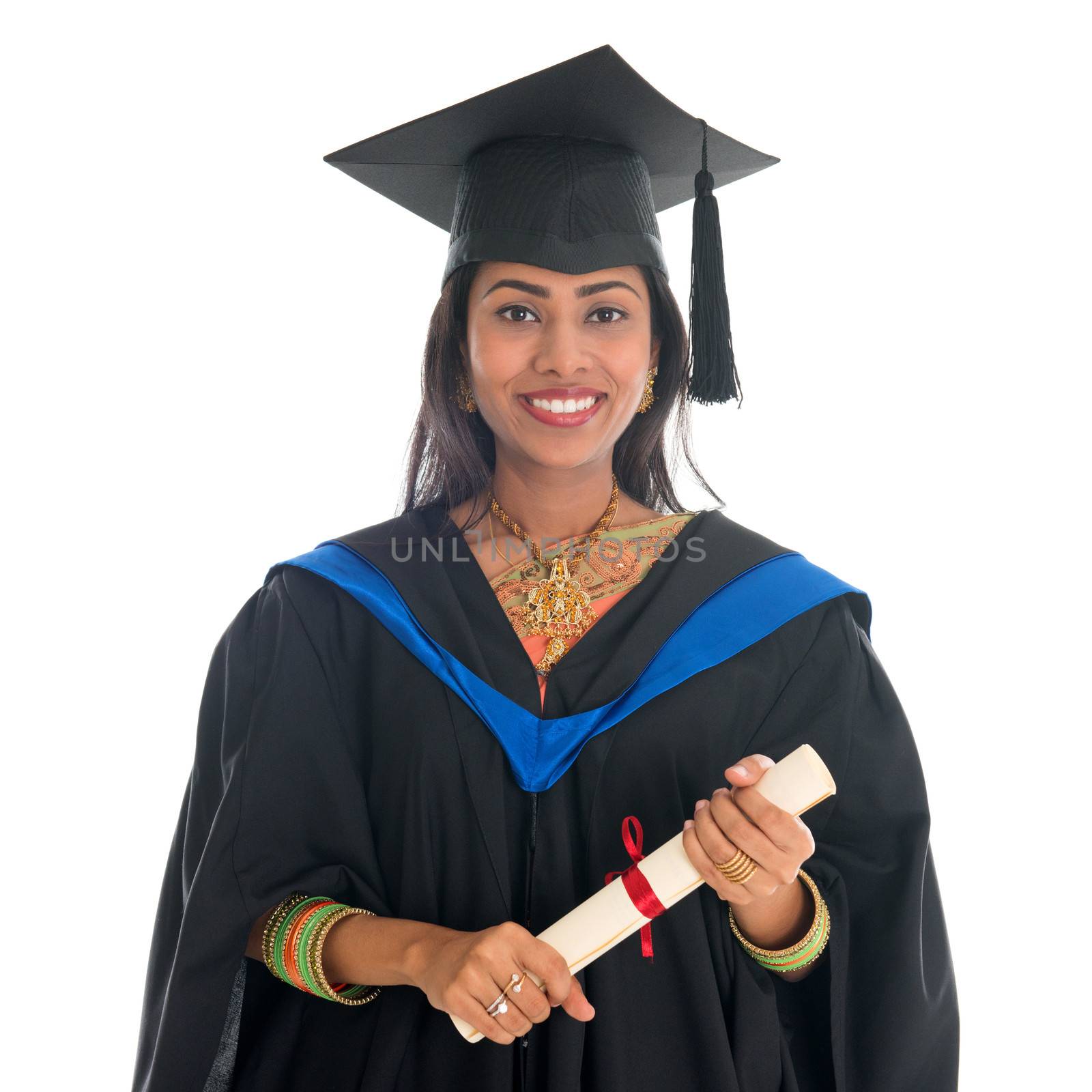 Happy Indian university student in graduation gown and cap holding diploma certificate. Portrait of mixed race Asian Indian and African American female model standing isolated on white background.