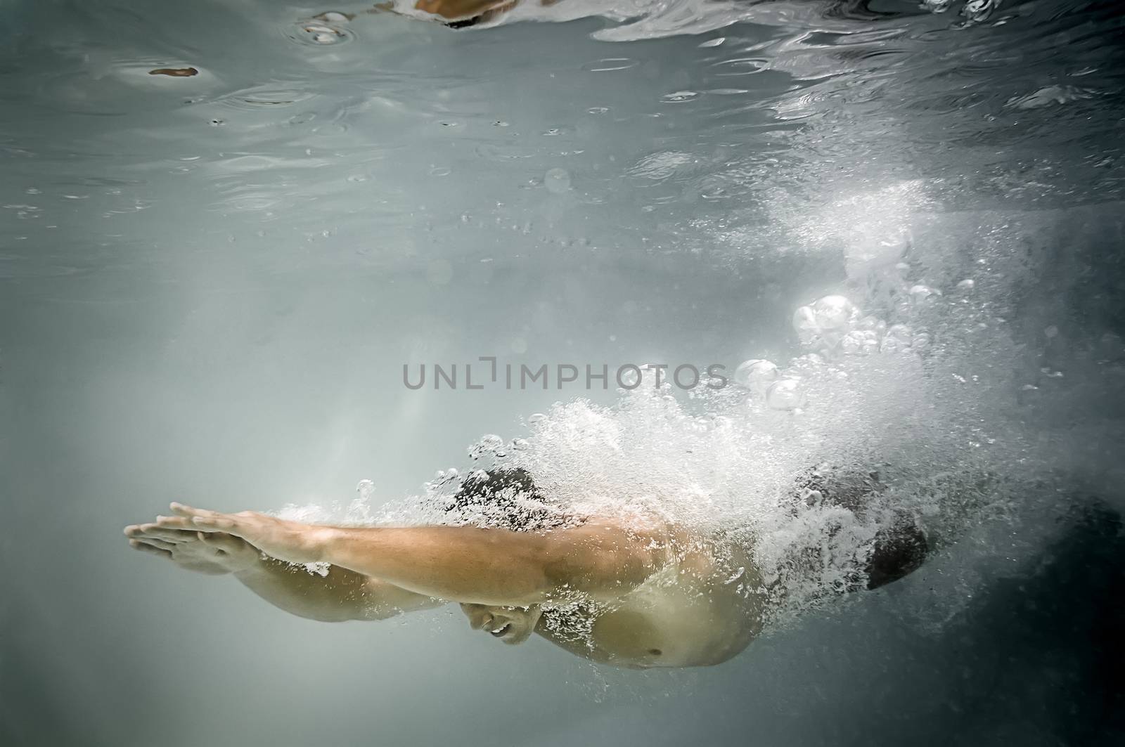 An image of a man diving in the pool with lots of air bubbles