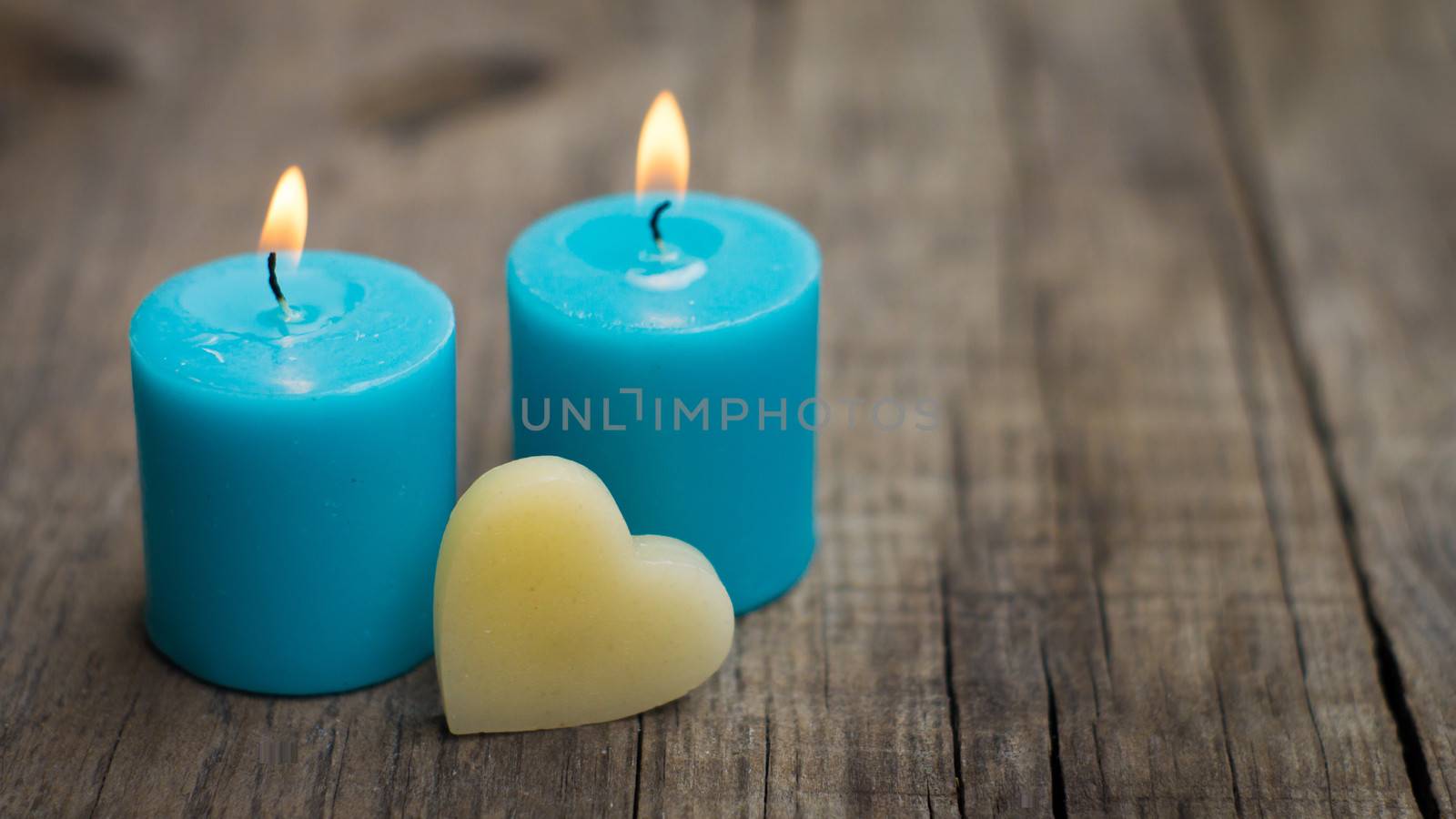 Blue burning candles with a heart on wood background.