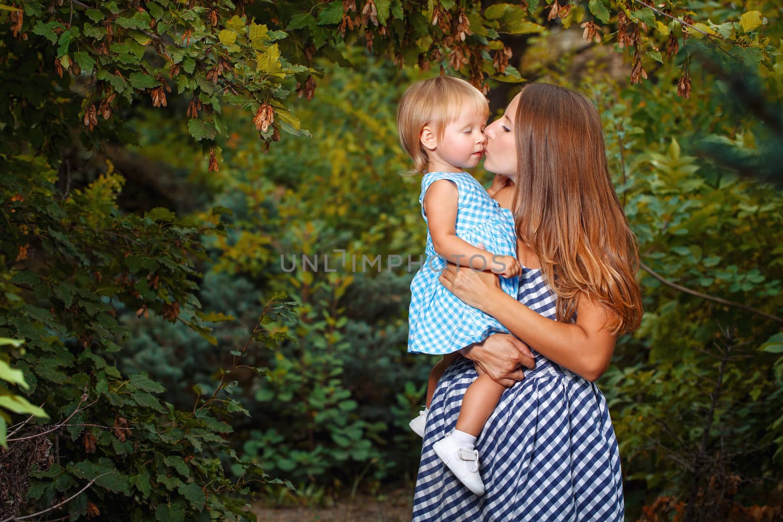 Mother holds daughter in his arms and kisses her on the cheek