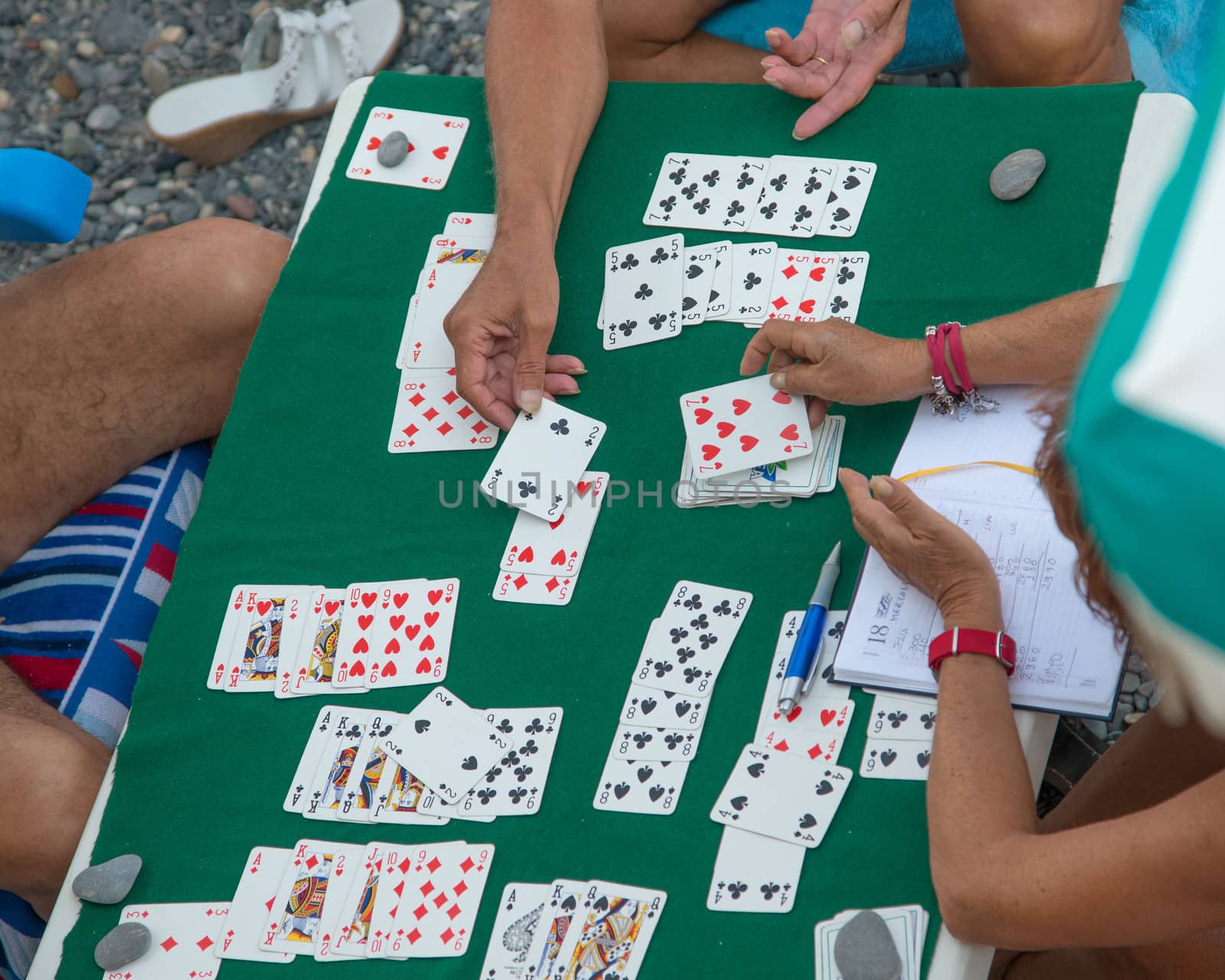 a group of friends playing cards under umbrella on the beach
