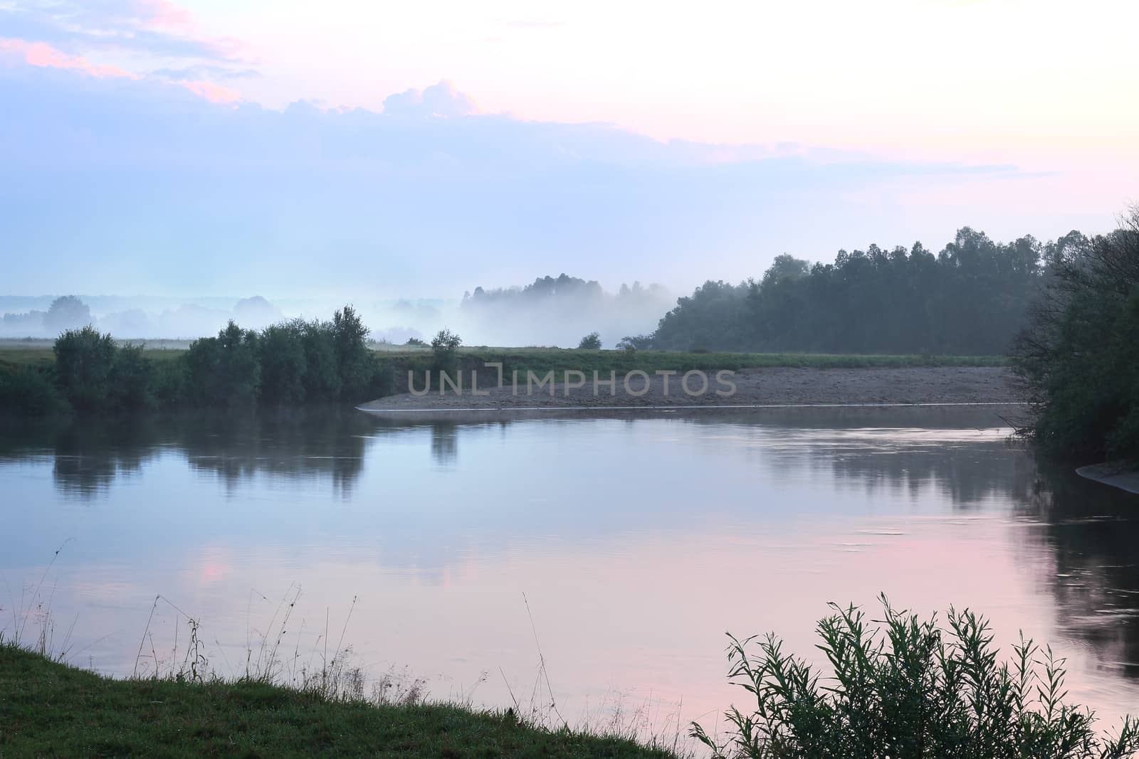 Landscape with the image of the river and the surrounding nature in the early misty morning.
